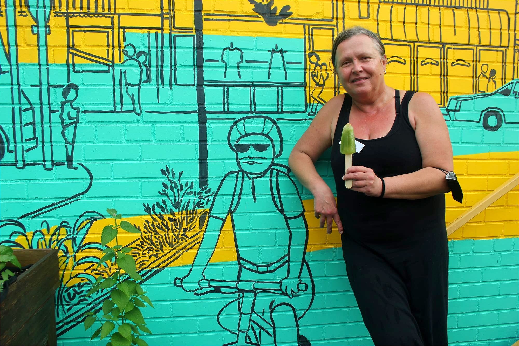 Mme Majewski pose devant une murale de Santropol Roulant. 