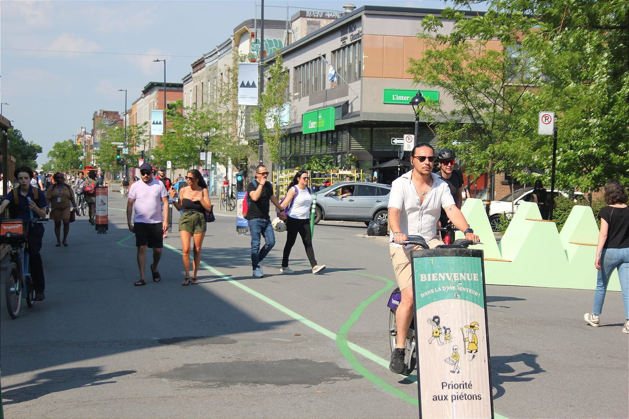 Un pancarte indique la priorité aux piétons, alors qu'on en aperçoit plusieurs en arrière-plan, devancés par trois cyclistes. 
