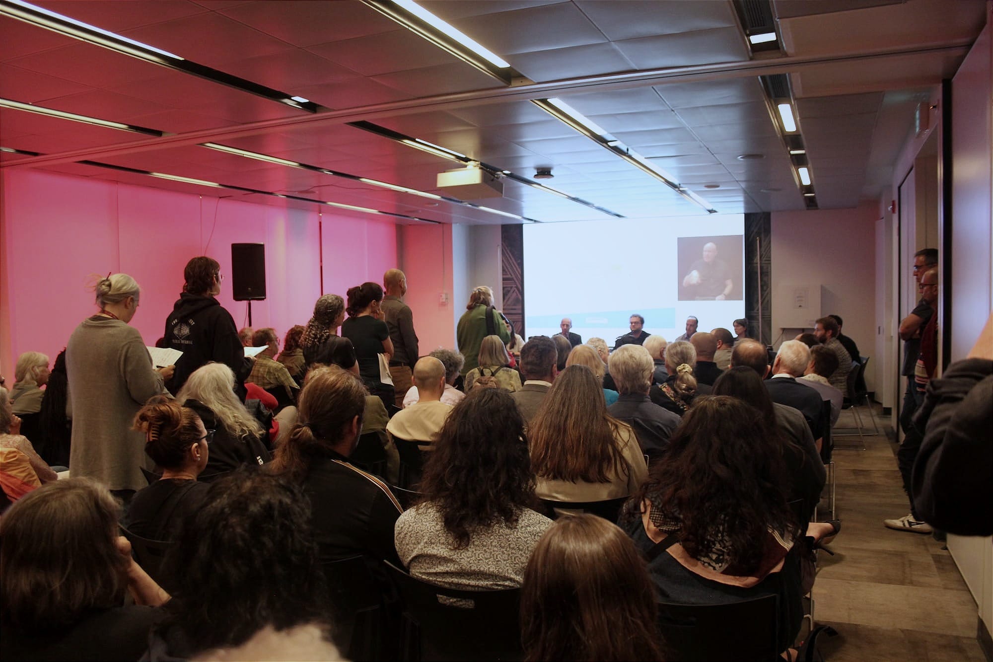Plusieurs rangées de sièges sont remplies et une file d'attente s'est formée derrière le micro voué aux questions du public.