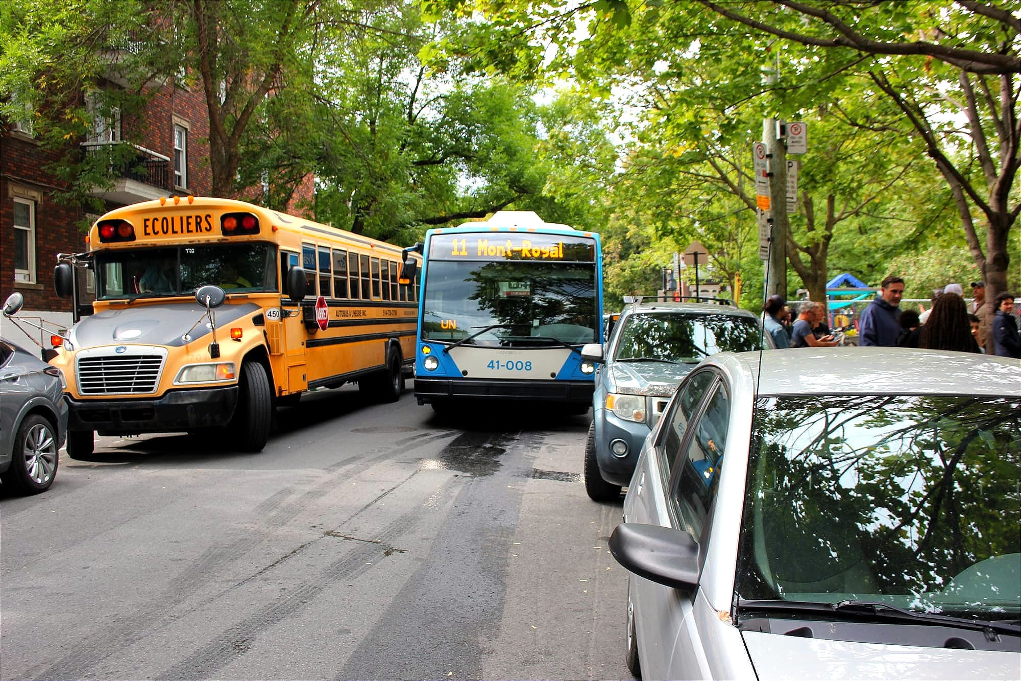 L'autobus de la STM, au centre de la voie, a peu d'espace entre un VUS à sa gauche et l'autobus scolaire à sa droite. 