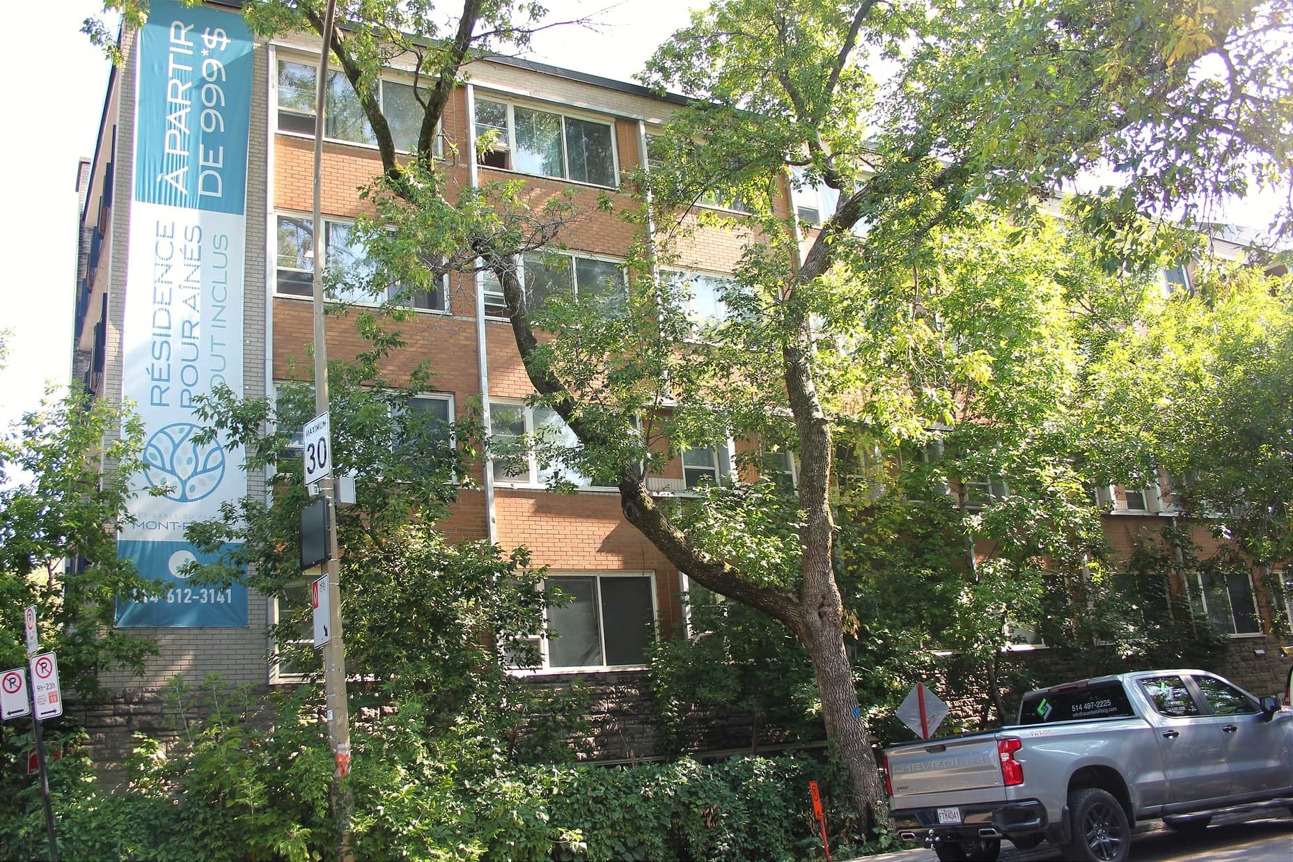 Vue de la bannière et du côté nord du bâtiment devant lequel on voit un camion et de la signalisation associés aux travaux. 