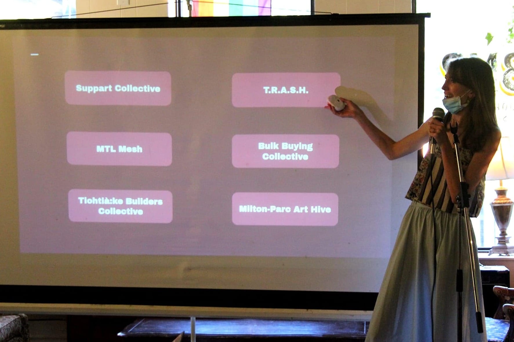 Mme Champagne tient un micro et pointe vers un tableau blanc sur lequel est projeté les noms des six projets. 