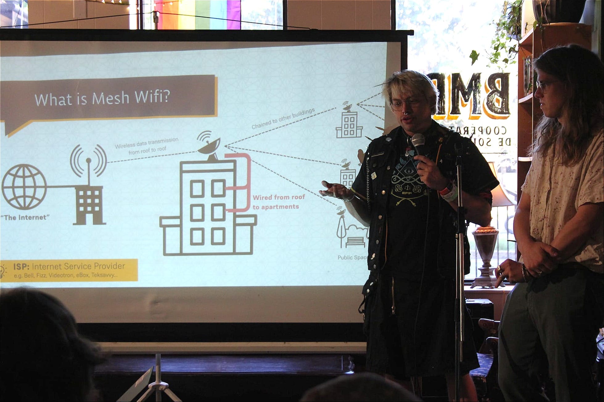 M. Ouelette tient un micro dans sa main, à côté d'une diapositive illustrant la distribution du signal du réseau de MTL Mesh.