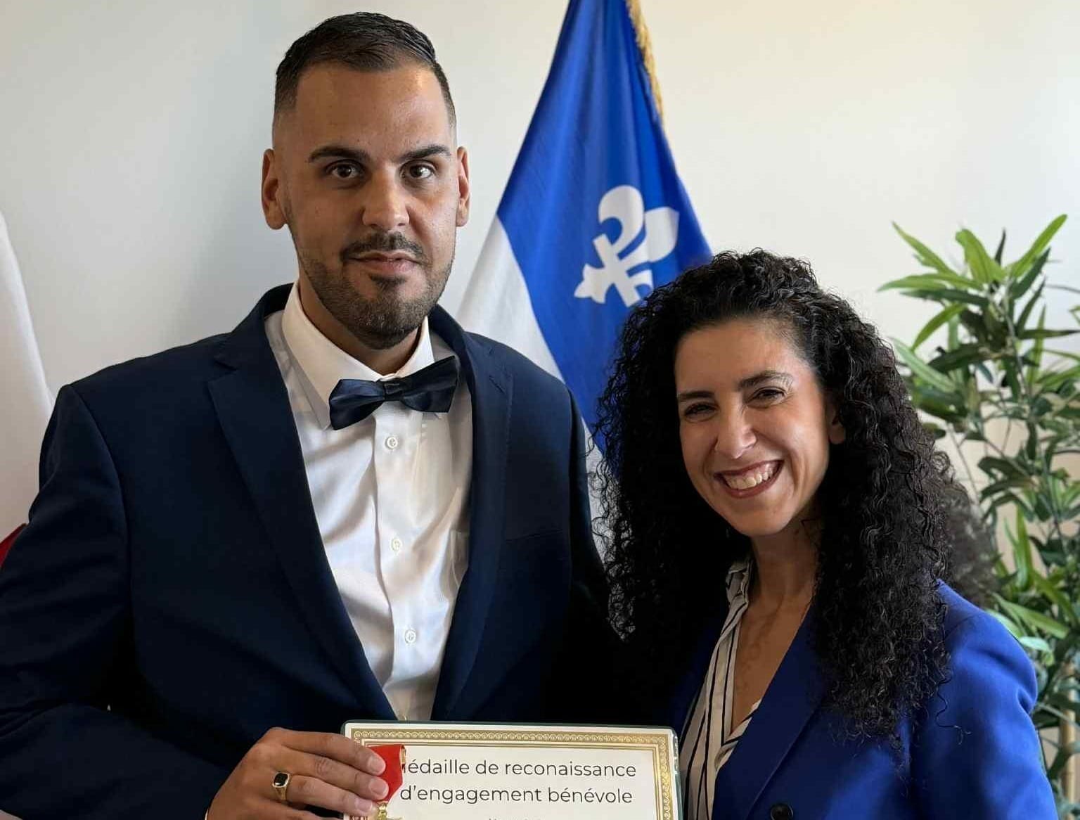 Un homme avec un nœud papillon tient un certificat et pose à côté de la députée Rachel Bendayan.