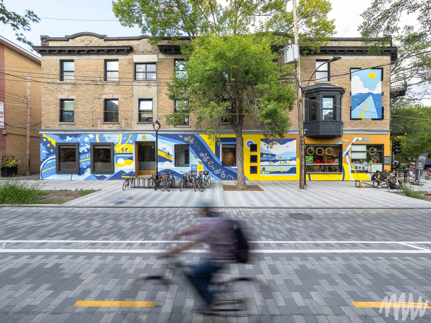 Derrière un cycliste flou, la photo présente une murale bleu et jaune.