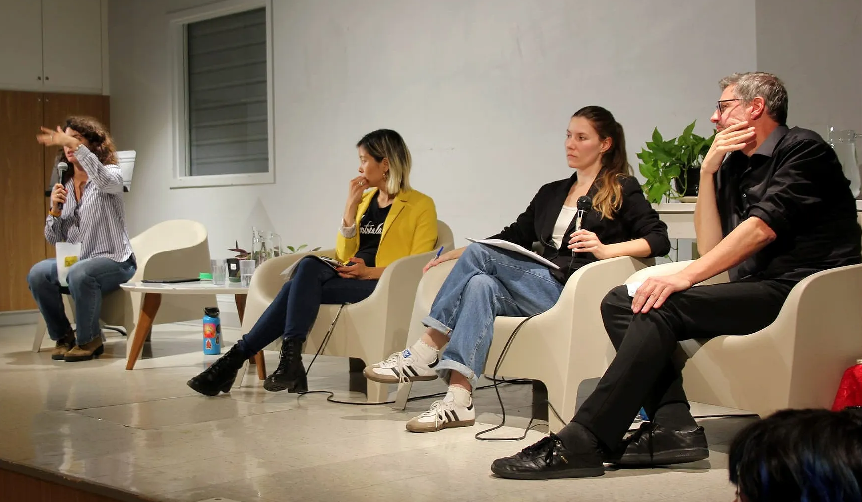 Les trois candidats assis à droite écoutent alors que l'animatrice de la soirée gesticule en parlant. 