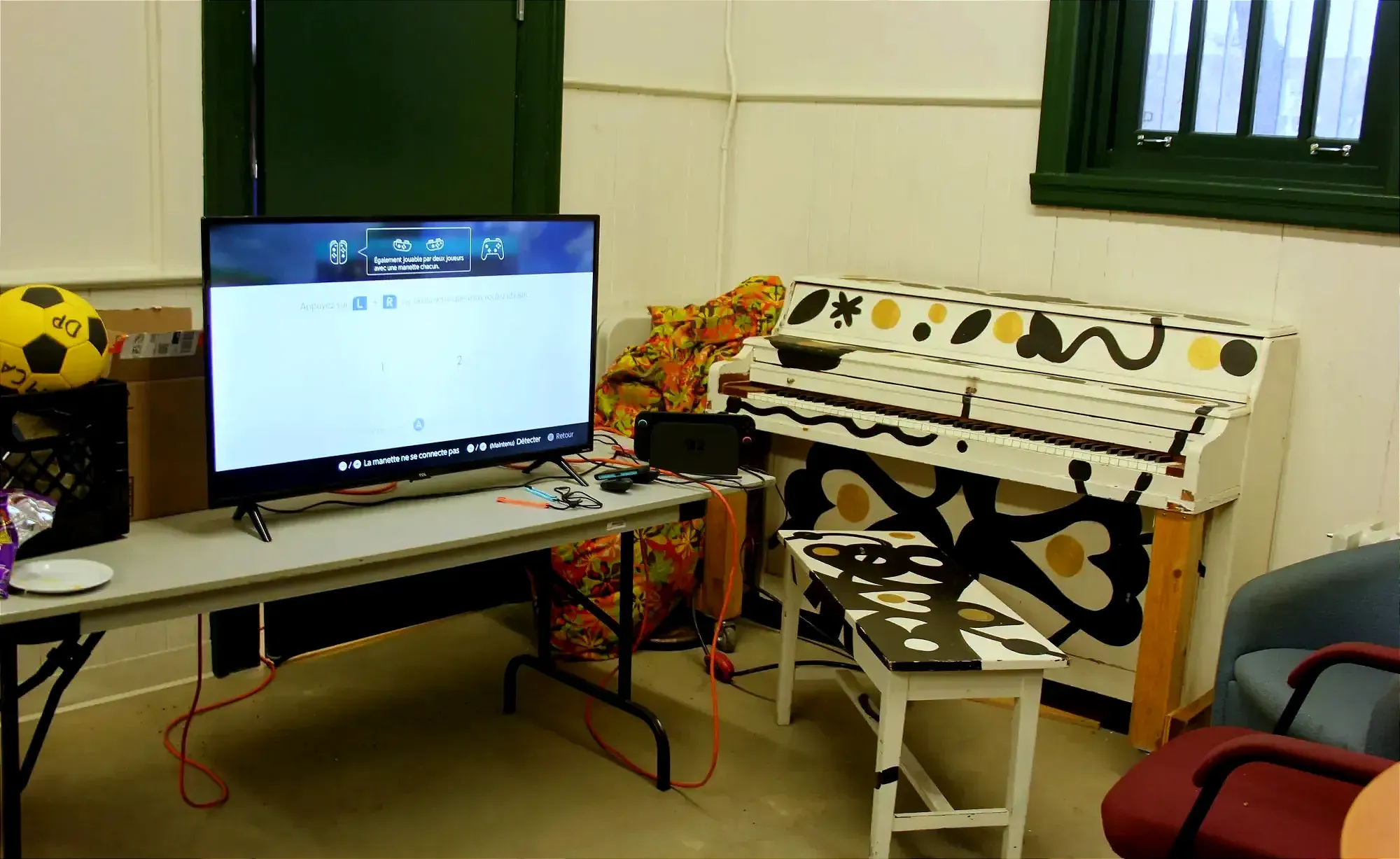 On y voit une télévision ouverte, branchée à un console de jeu vidéo, ainsi qu'un piano qui longe le mur.