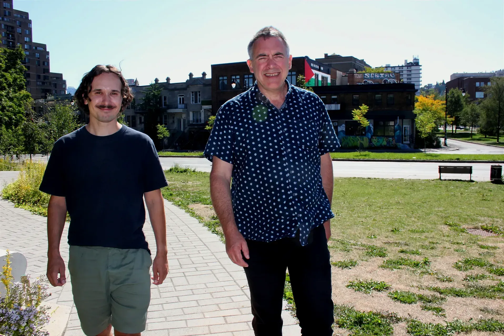 MM. Fortin et Norris marchent en direction de la caméra, sur le chemin du parc Lucia-Kowaluk, faisant dos à l'avenue du Parc.