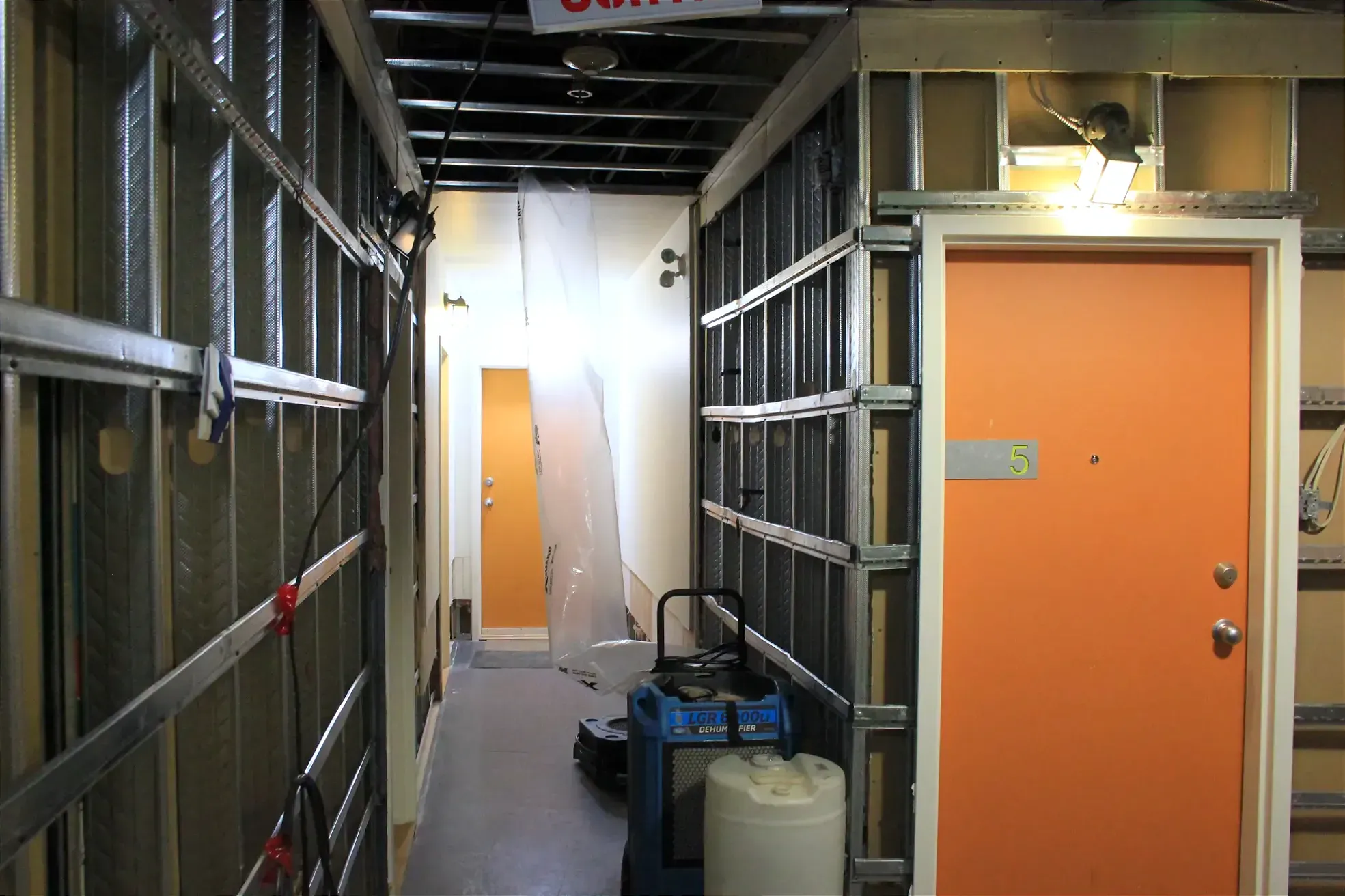 On voit les poutres métalliques, ainsi qu'un déshumidificateurs au milieu d'un corridor. 