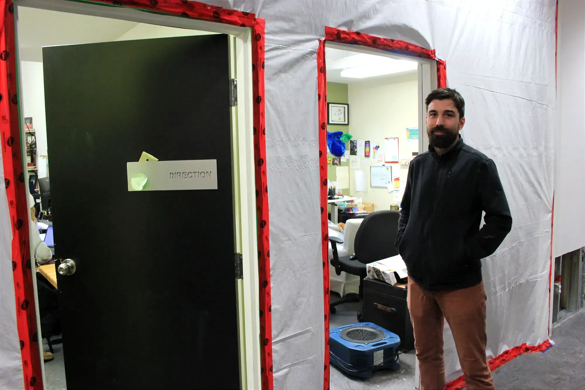 Le directeur général pose devant les bureaux de la direction de l'organisme. Les murs sont plastifiés. 