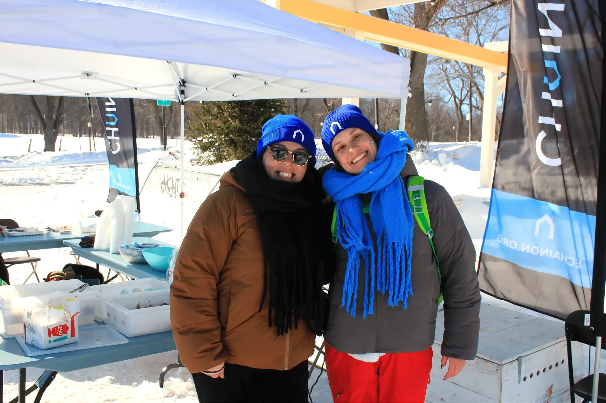Les deux dames posent pour la caméra en souriant, avec des tuques bleues du Chaînon sur la tête. 