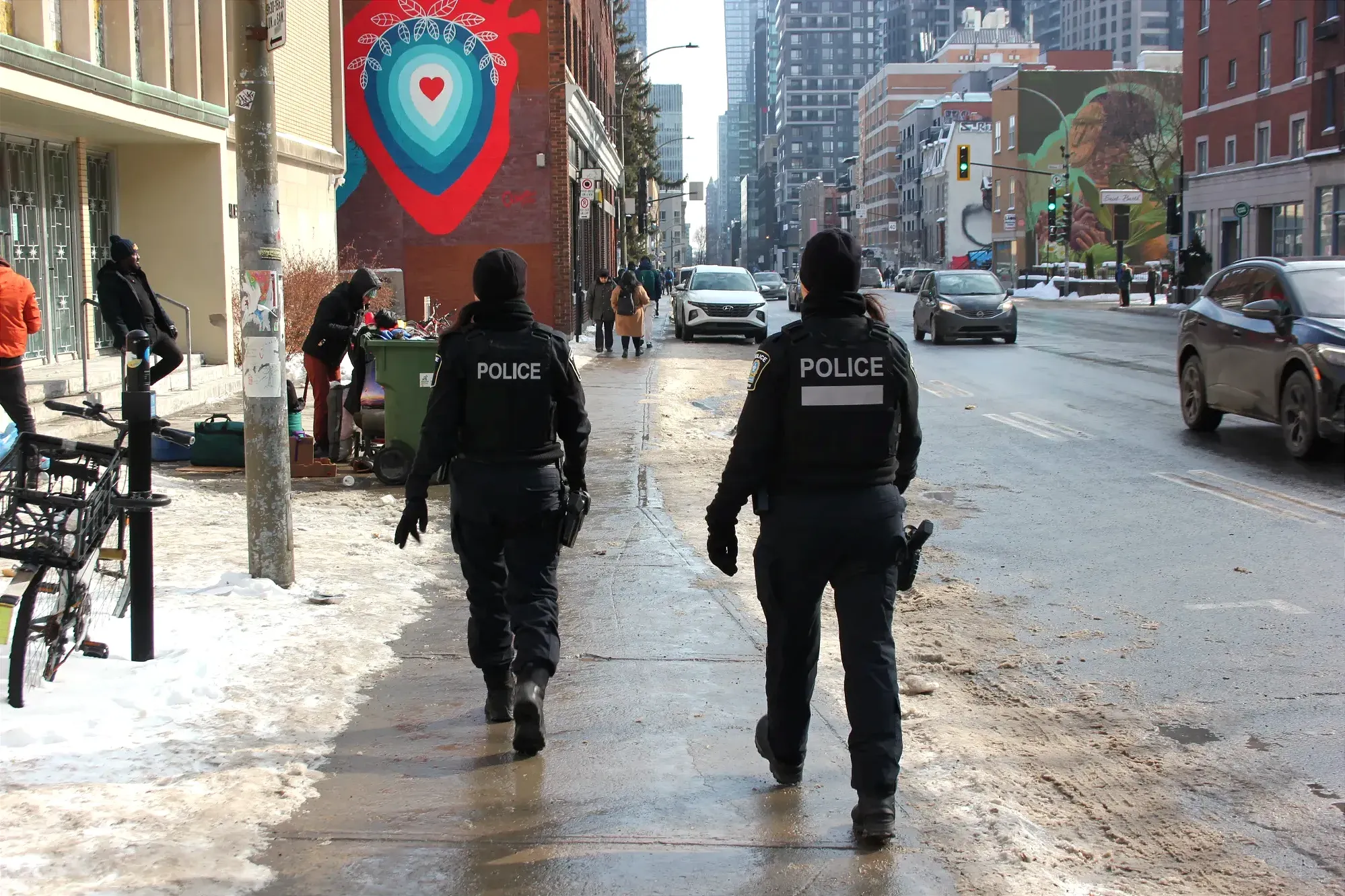On voit les deux agentes de dos, alors qu'elle s'approchent de l'entrée de l'organisme La porte ouverte.