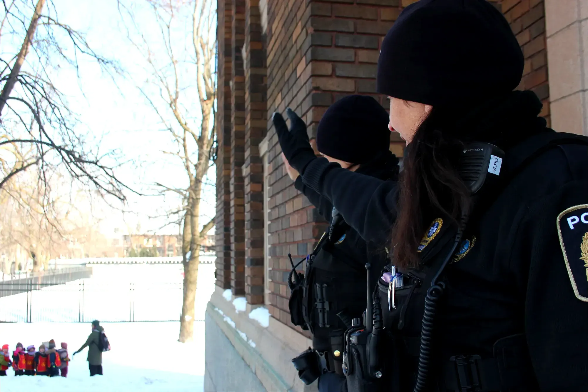 On voit le groupe d'enfants flou, au loin près de la clôture de la piscine du parc, alors que les deux policières regardent dans leur direction, tout près de la caméra, à la droite du cadre.