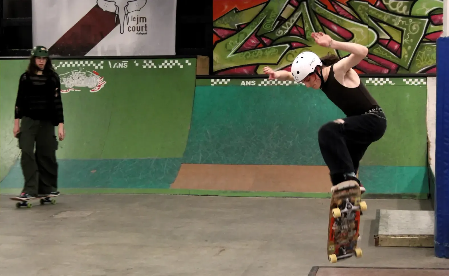 Scout se lance sur une plateforme surélevée avec sa planche sous le regard de Violet.