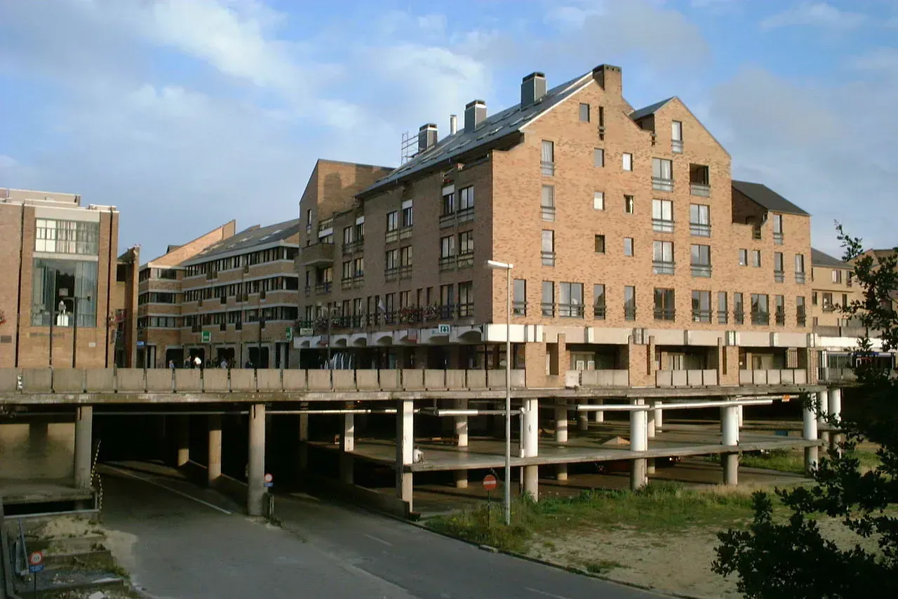 On voit une route qui passe de l'extérieur à un passage souterrain, qui comprend deux étages de stationnement. Des édifices sont soutenus au-dessus de ces structures.