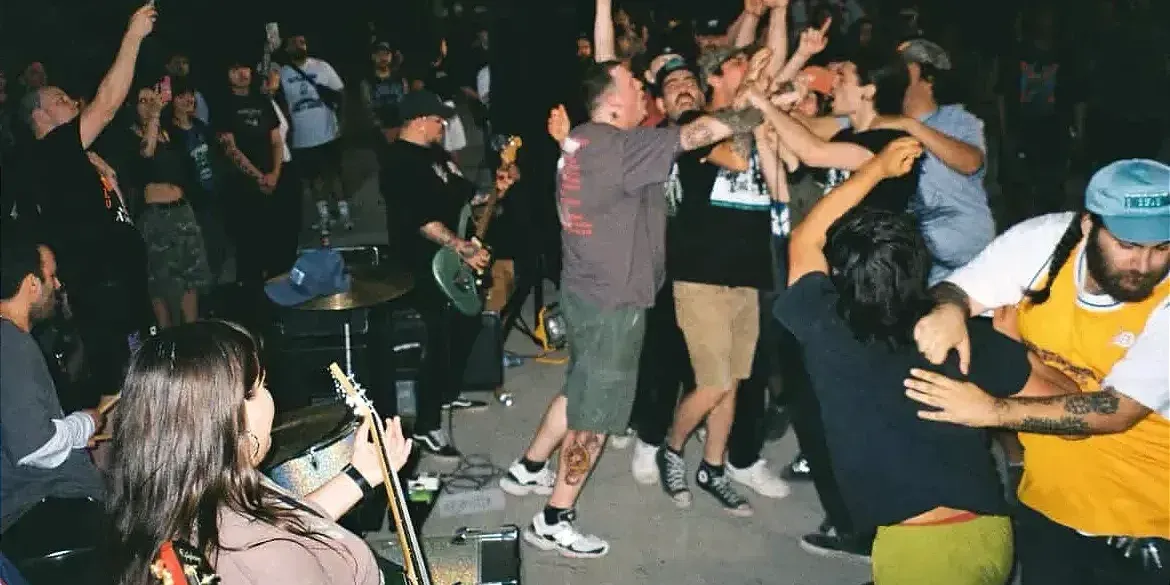 On voit les musiciens de dos alors que les spectateurs s'agglutinent entre eux. 