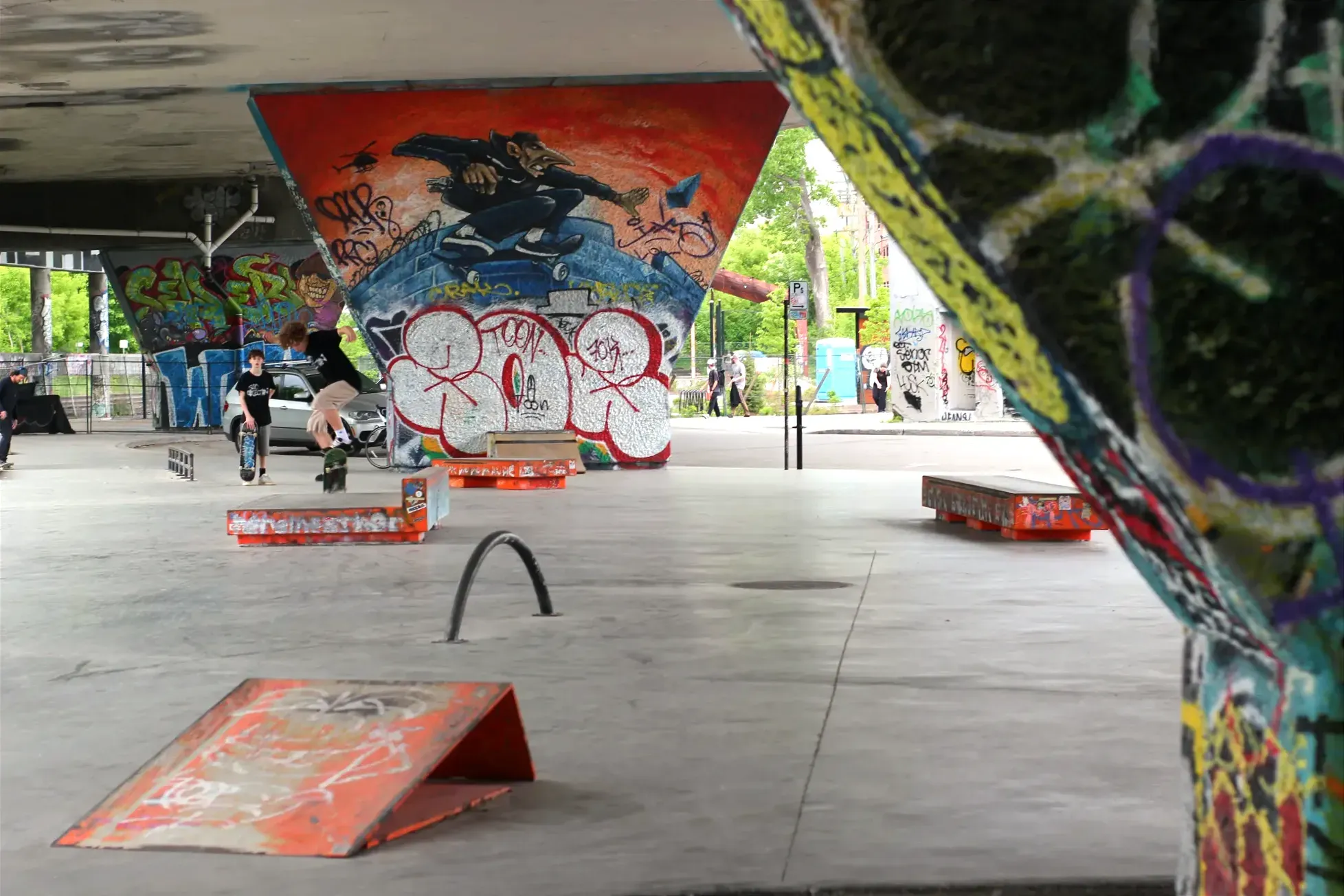 On voit des planchistes au loin qui s'exercices à proximité des piliers du viaduc, qui sont recouverts de couleurs.
