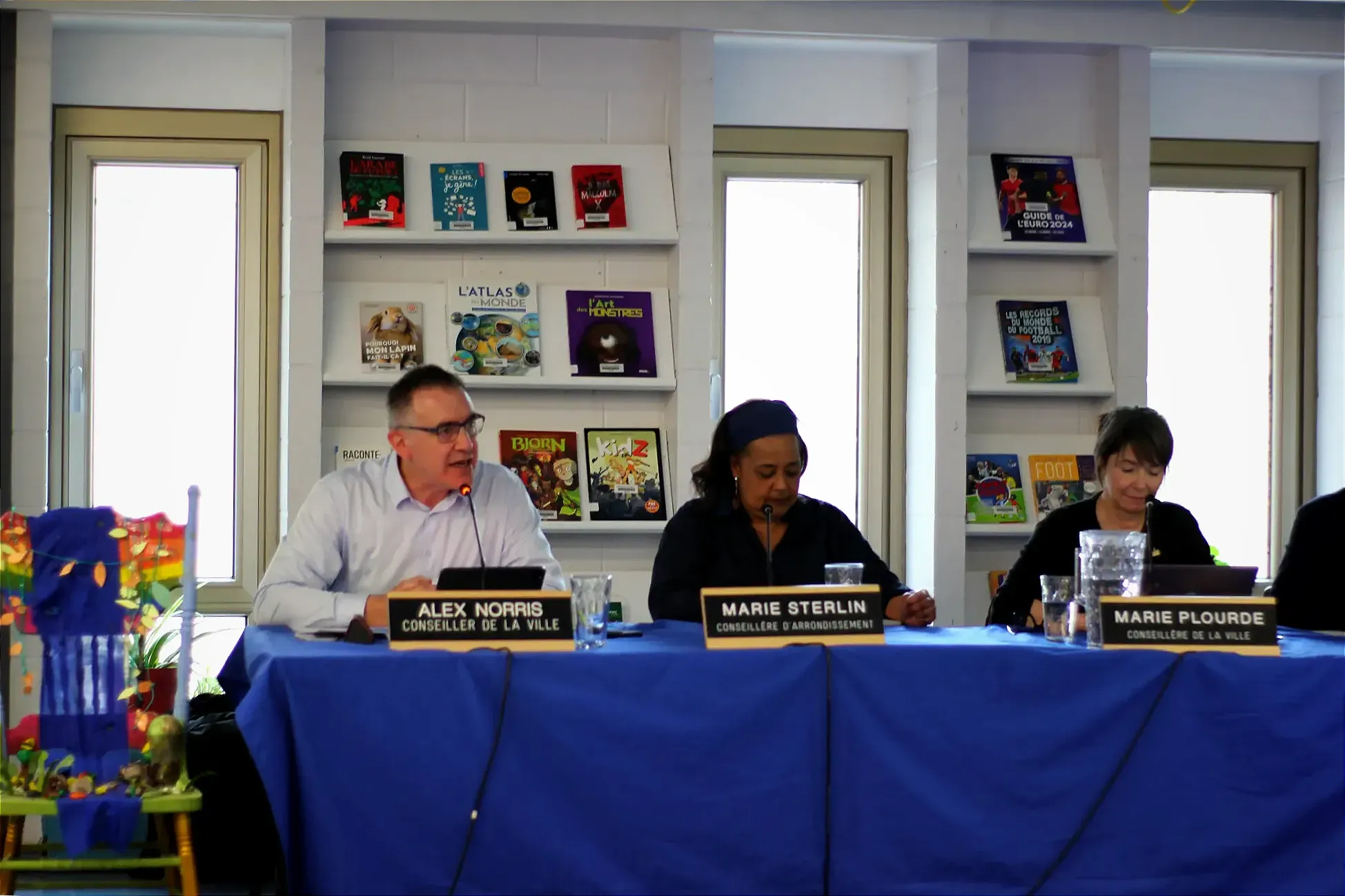 M. Norris prend la parole aux côté de Marie Sterlin et Marie Plourde, lors de la séance du conseil d'arrondissement, dans la bibliothèque de l'école Jeanne-Mance. 