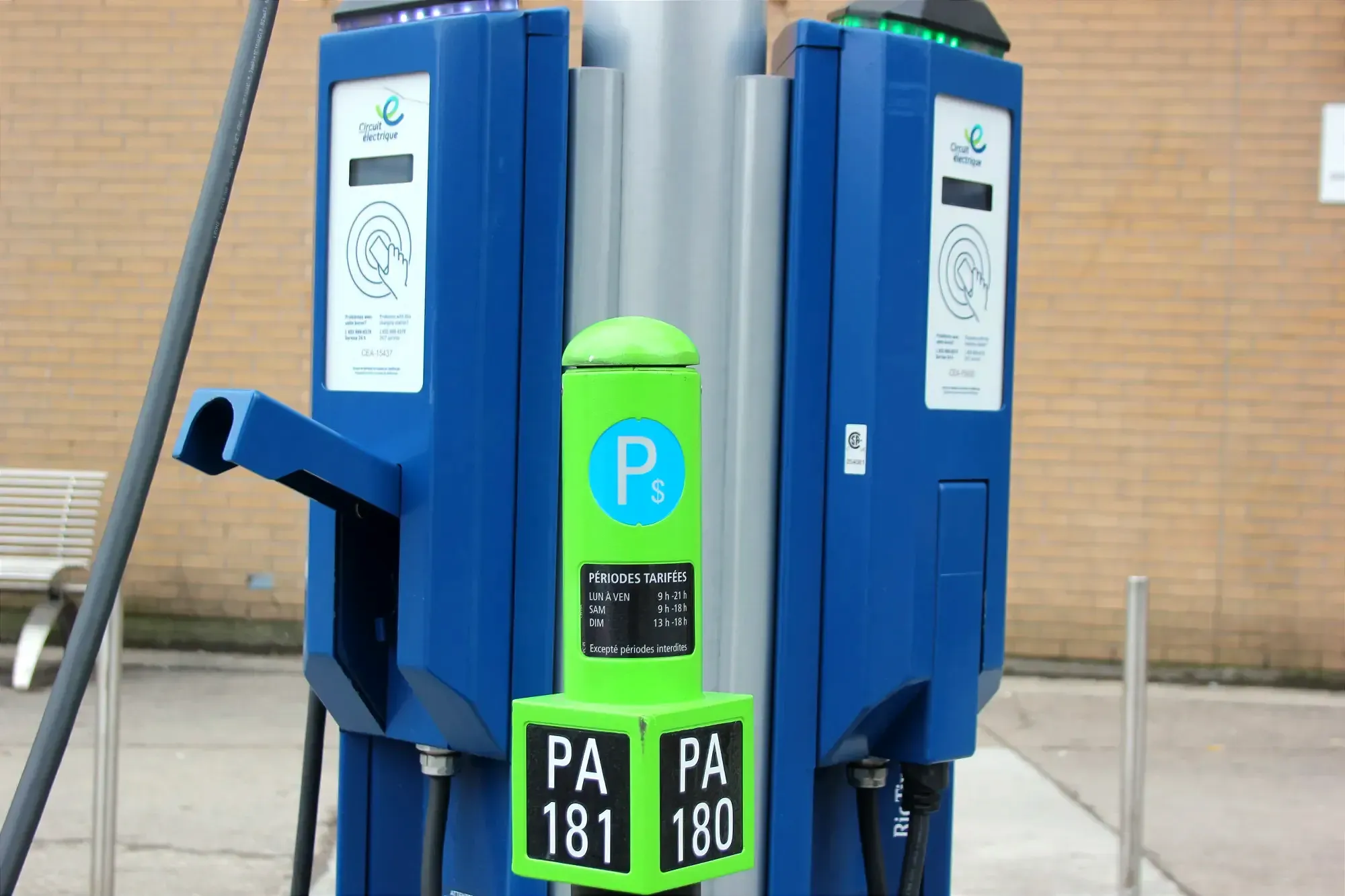 Un poteau de parcomètre au sommet vert est installé devant une borne de recharge. 