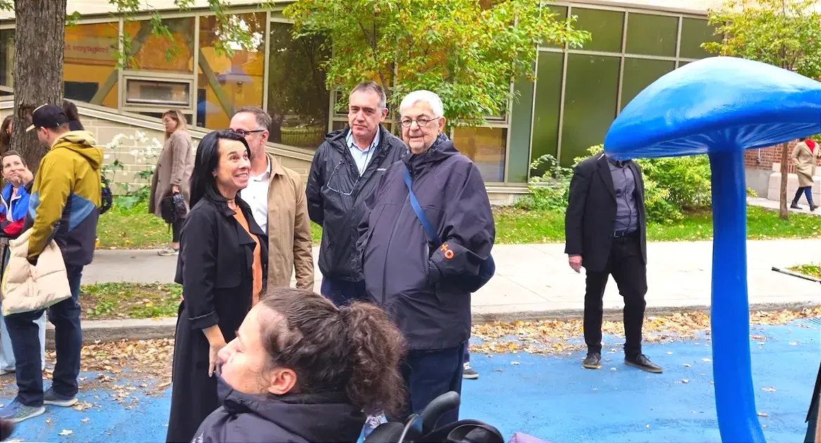 Photo tirée de l'inauguration de 2024 de la placé-école. On peut voir une forme de champignon géant bleu s'étirer à la gauche de Michel Tremblay.