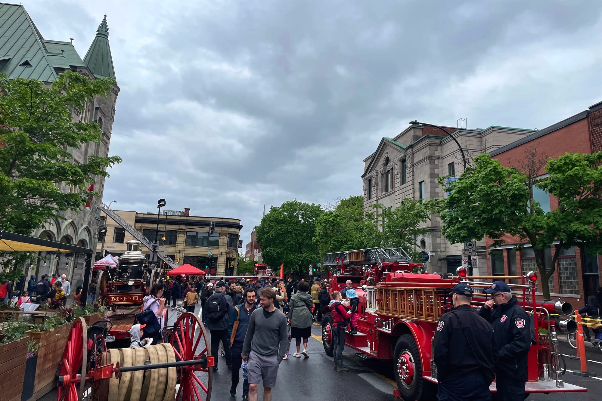 Plusieurs personnes se balades sur une avenue Laurier humide, où plusieurs véhicules et outils de pompiers sont exposés.