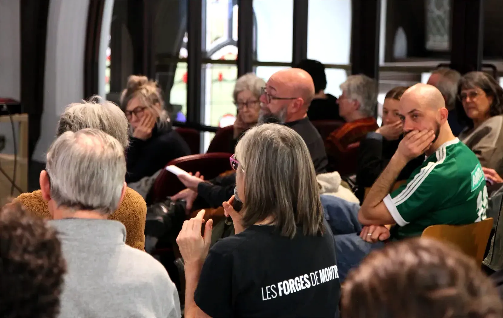 Une dame de dos, prend la parole au micro, alors que plusieurs autres membres du public se retournent dans sa direction.
