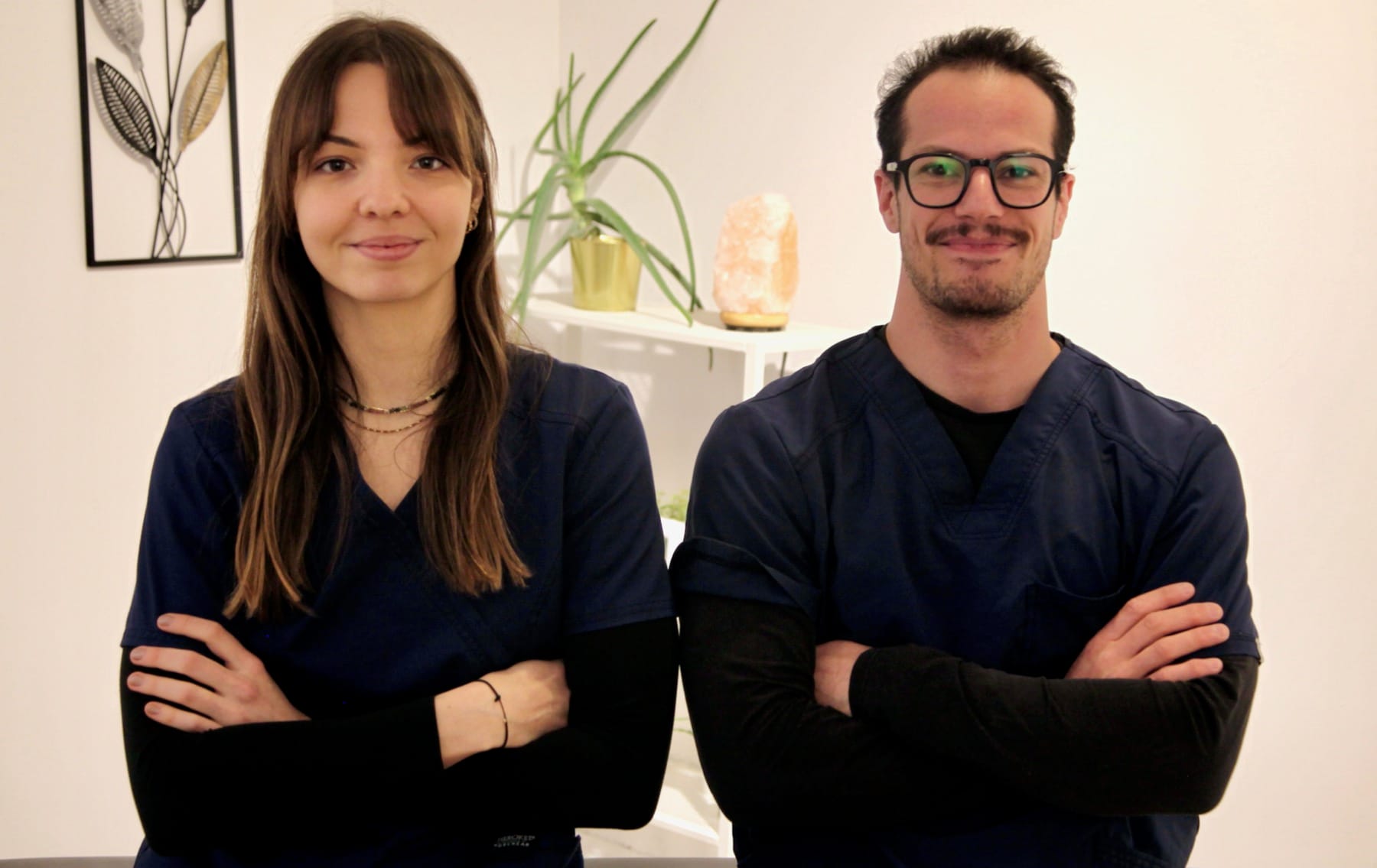 Une femme et un homme posent côte à côte dans une salle décorée avec des plantes, des cadres et une lampe.