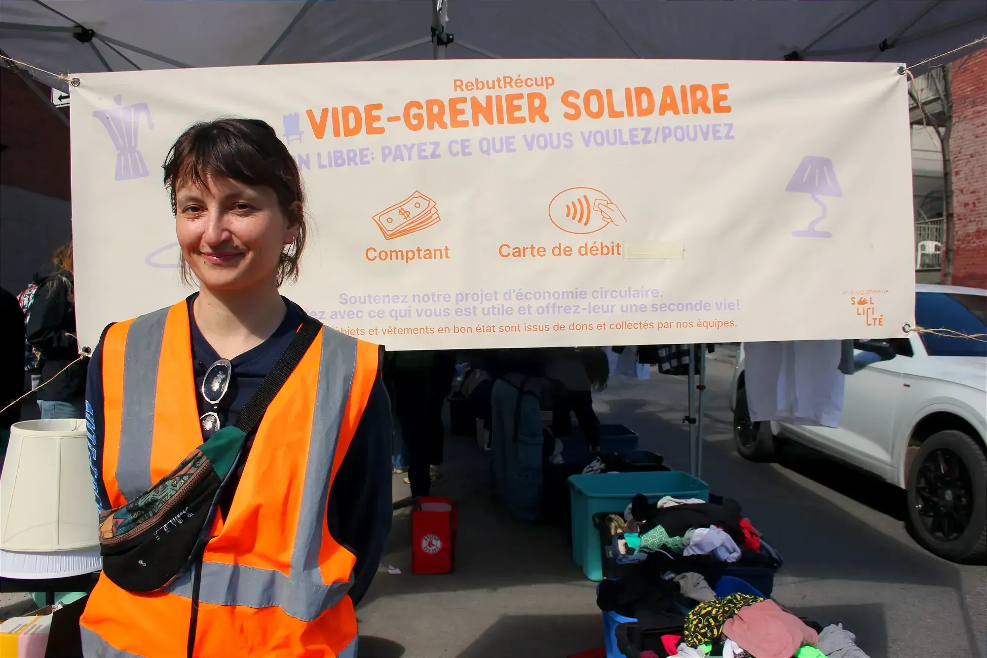 Mme Lebihain pose devant une banderole du vide-grenier solidaire.