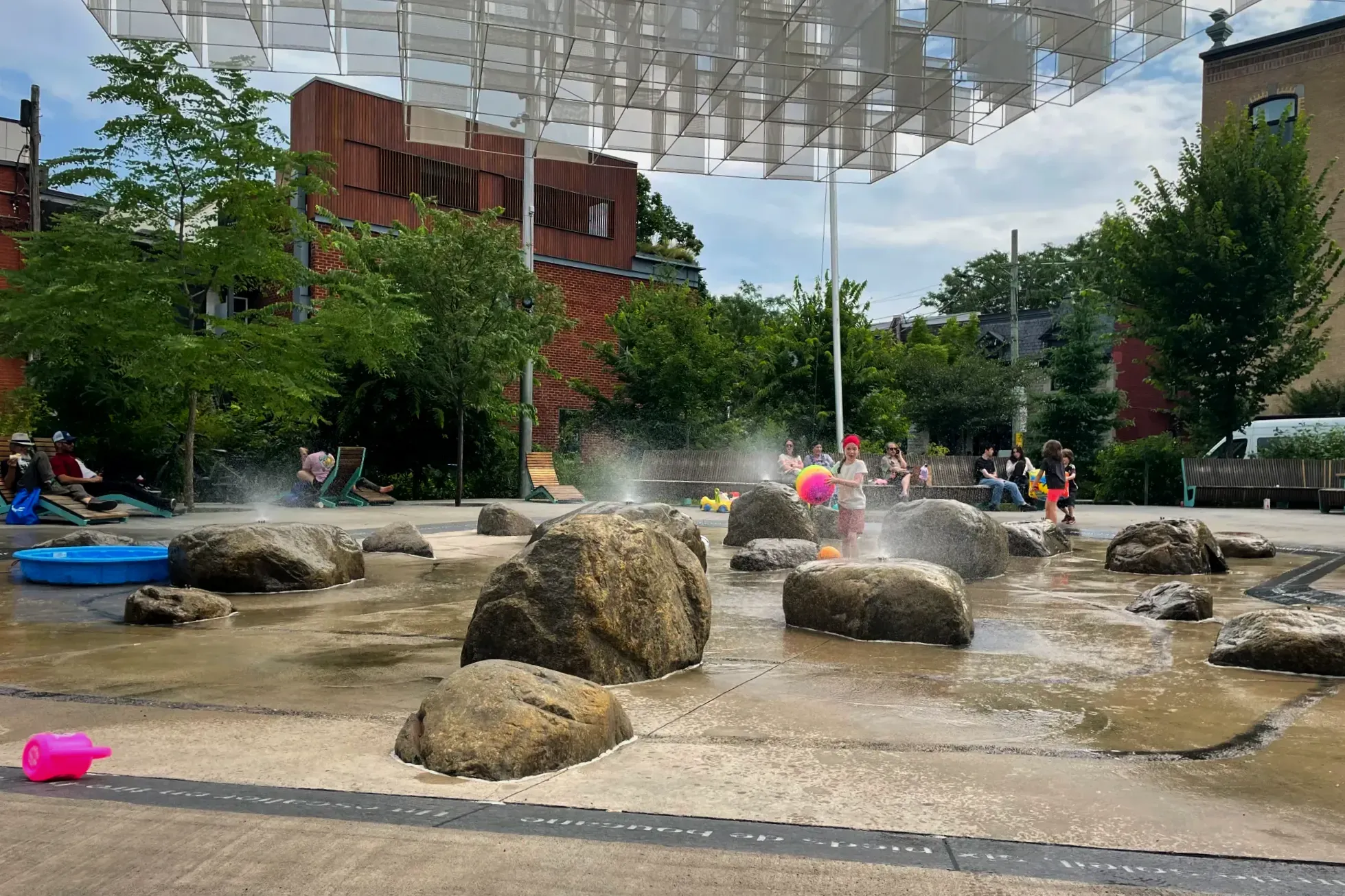 Des enfants jouent parmi les roches et les jets de bruine de la place des Fleurs-de-Macadam.