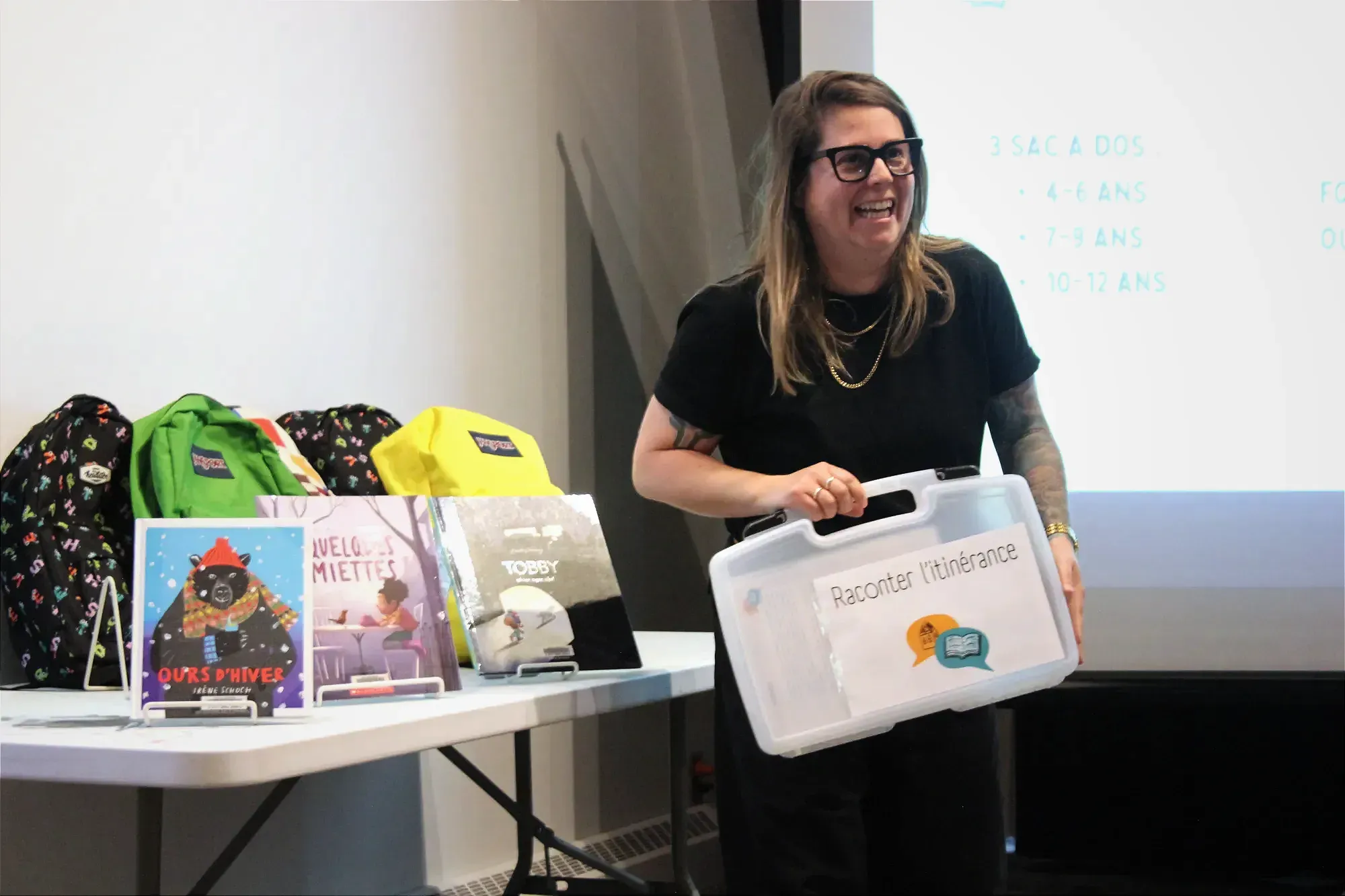 Mme Dalpé tient une valise sur laquelle on peut lire «Raconter l'itinérance», à côté d'une table où l'on peut voir quelques livres et sacs à dis liés au projet.