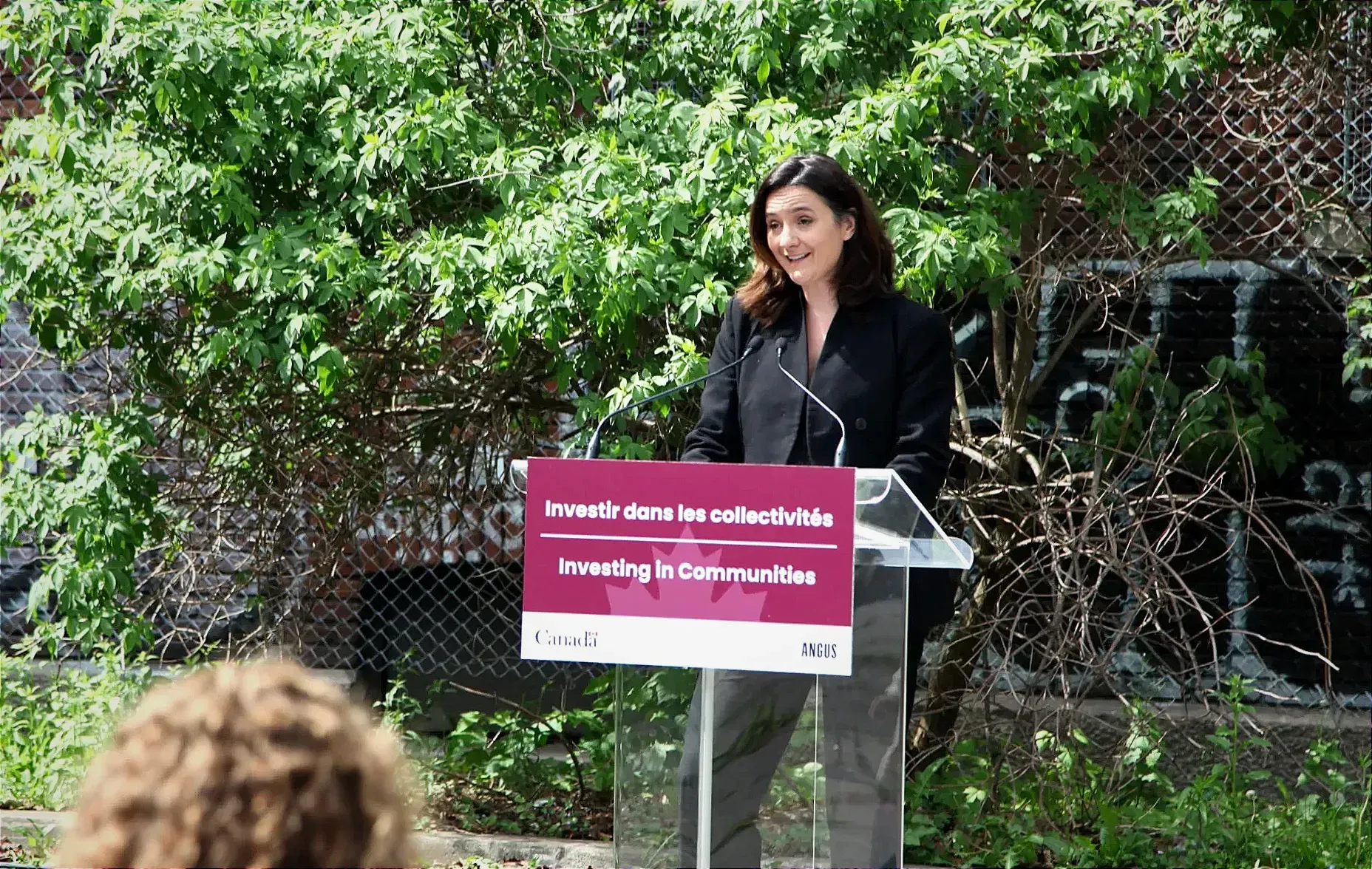 Mme Hudon-Huot s'exprime derrière un podium placé dans le stationnement arrière du bâtiment de l'ancienne école Luke Callaghan.