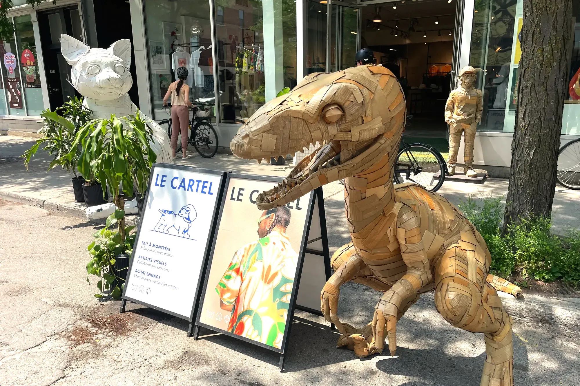Un genre de sculpture en forme de vélociraptor se trouve à la droite de pancarte annonçant le magasin Le Cartel. Un chat et un singe peuvent être aperçus plus loin.