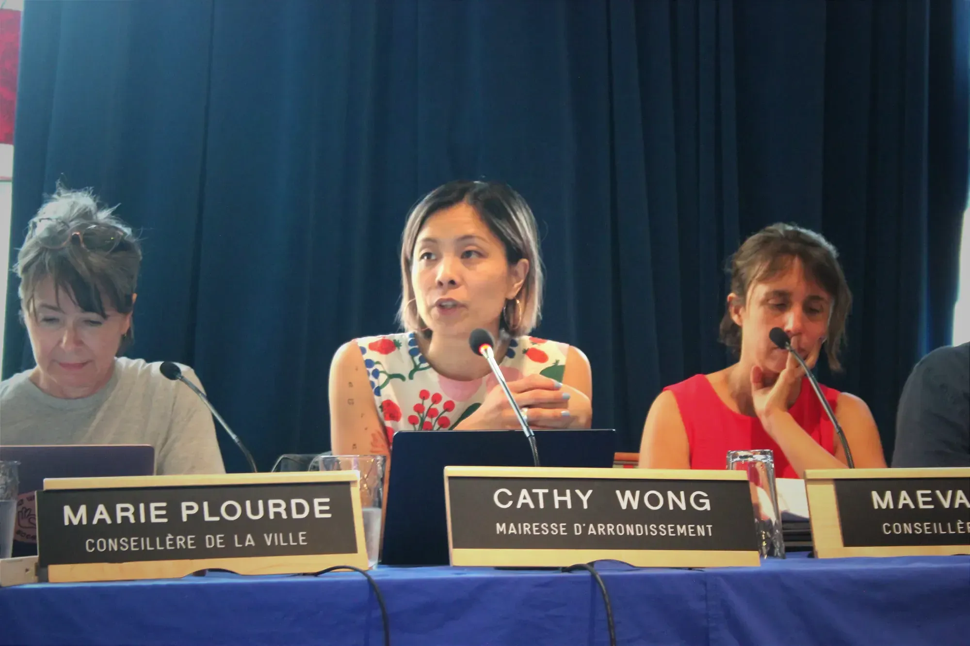 Mme Wong s'exprime au micro, lors de la séance du conseil d'arrondissement, entourée des conseillères de la Ville, Marie Plourde et Maeva Vilain.
