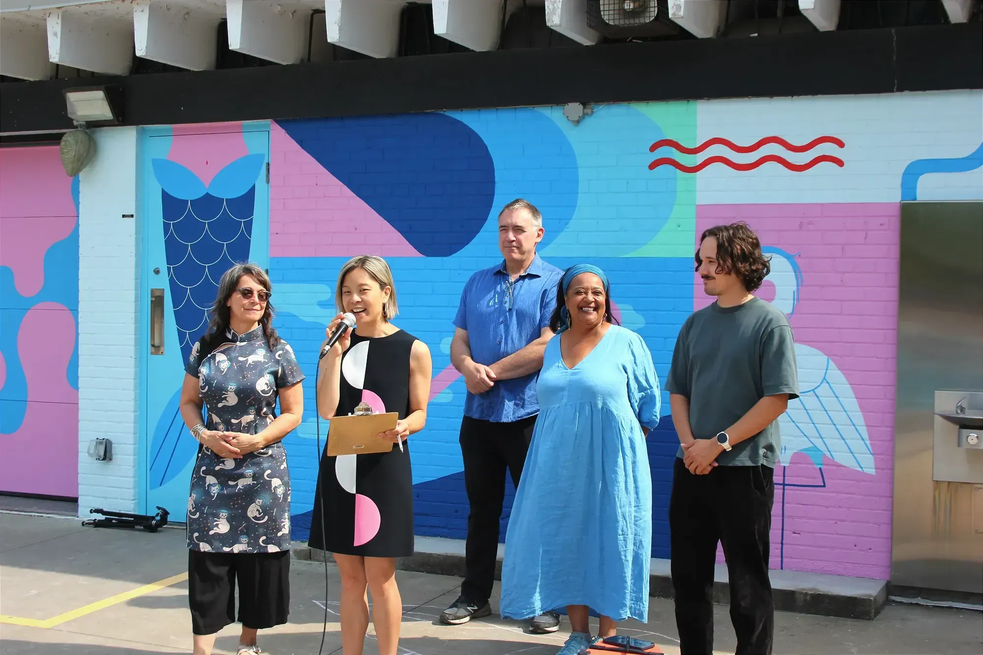 Cathy Wong prend la parole (et le micro) devant la murale de Not So Evil, en compagnie de Marie Plourde, Alex Norris, Marie Sterlin et Gabriel Fortin.