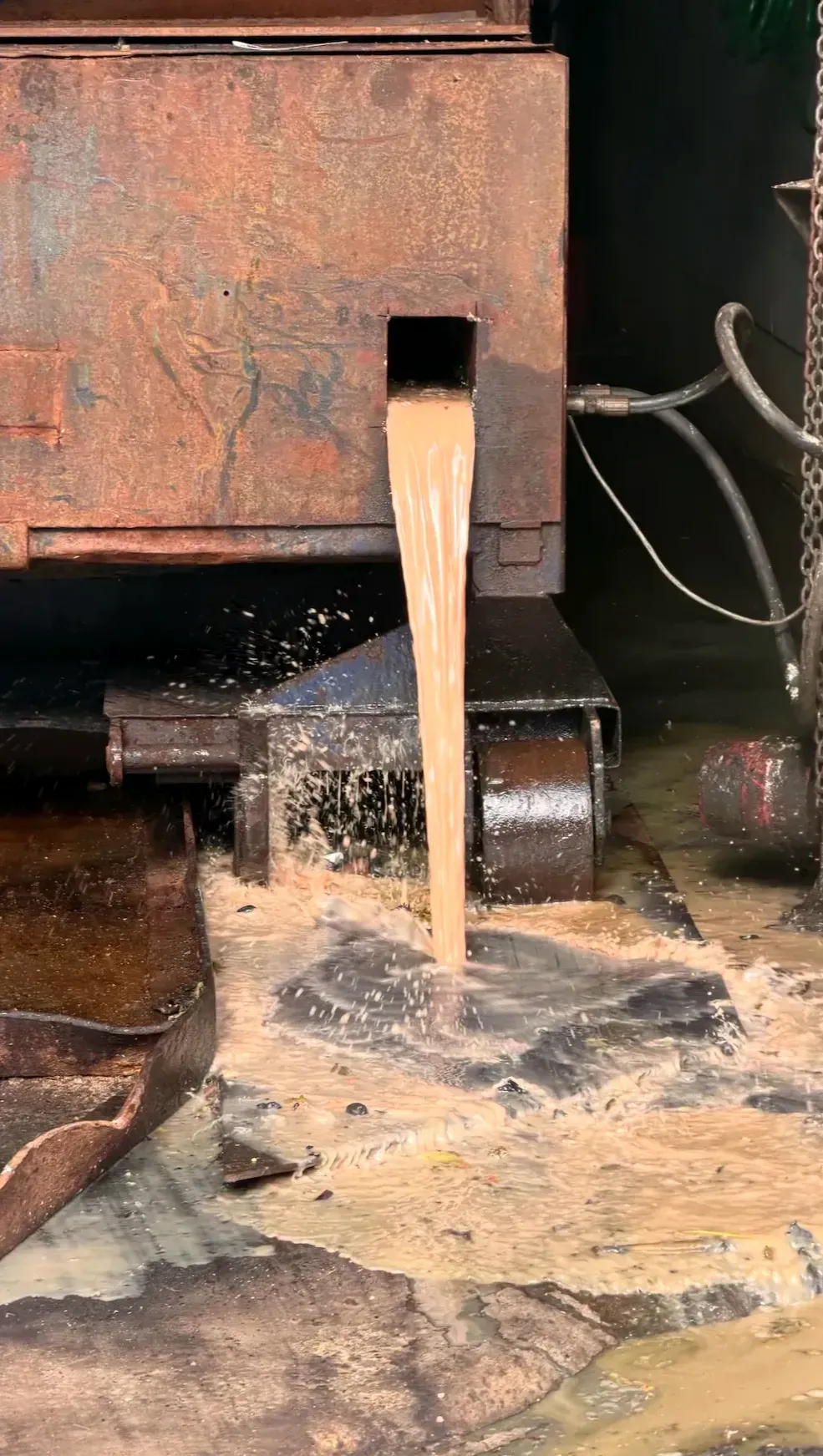 Un imposant jet brunâtre sort d'un trou du compacteur et se déverse sur le sol. Le liquide s'éparpille un peu partout.