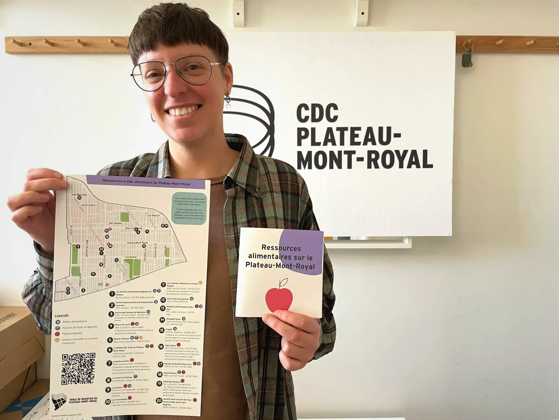 Mme Ingenito tient les documents dans ses mains, debout, devant une affiche de la CDC Plateau-Mont-Royal.