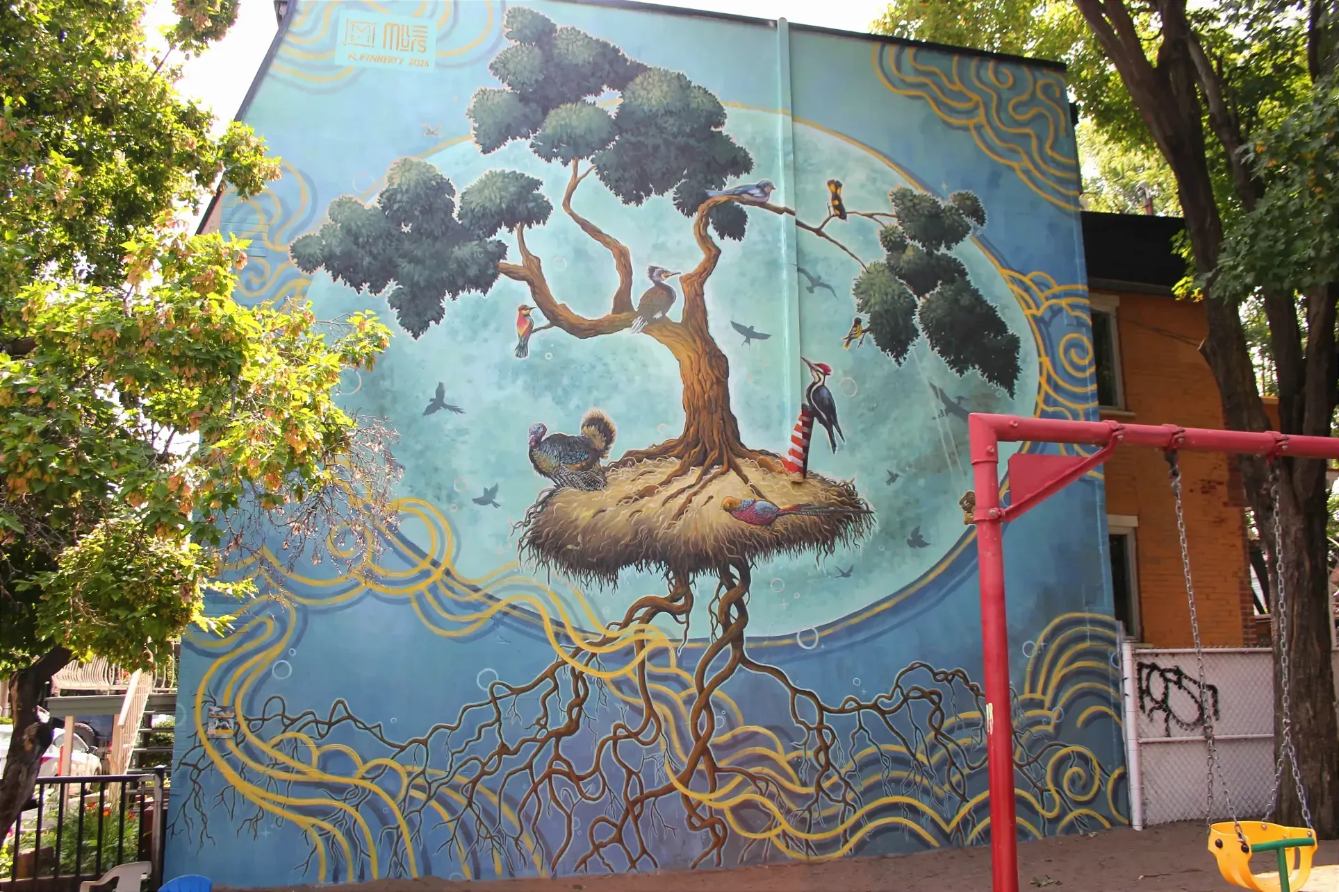 Derrière les balançoires du parc, un arbre s'élance dans les airs, avec des oiseaux de toutes sortes qui se tiennent aux alentours.