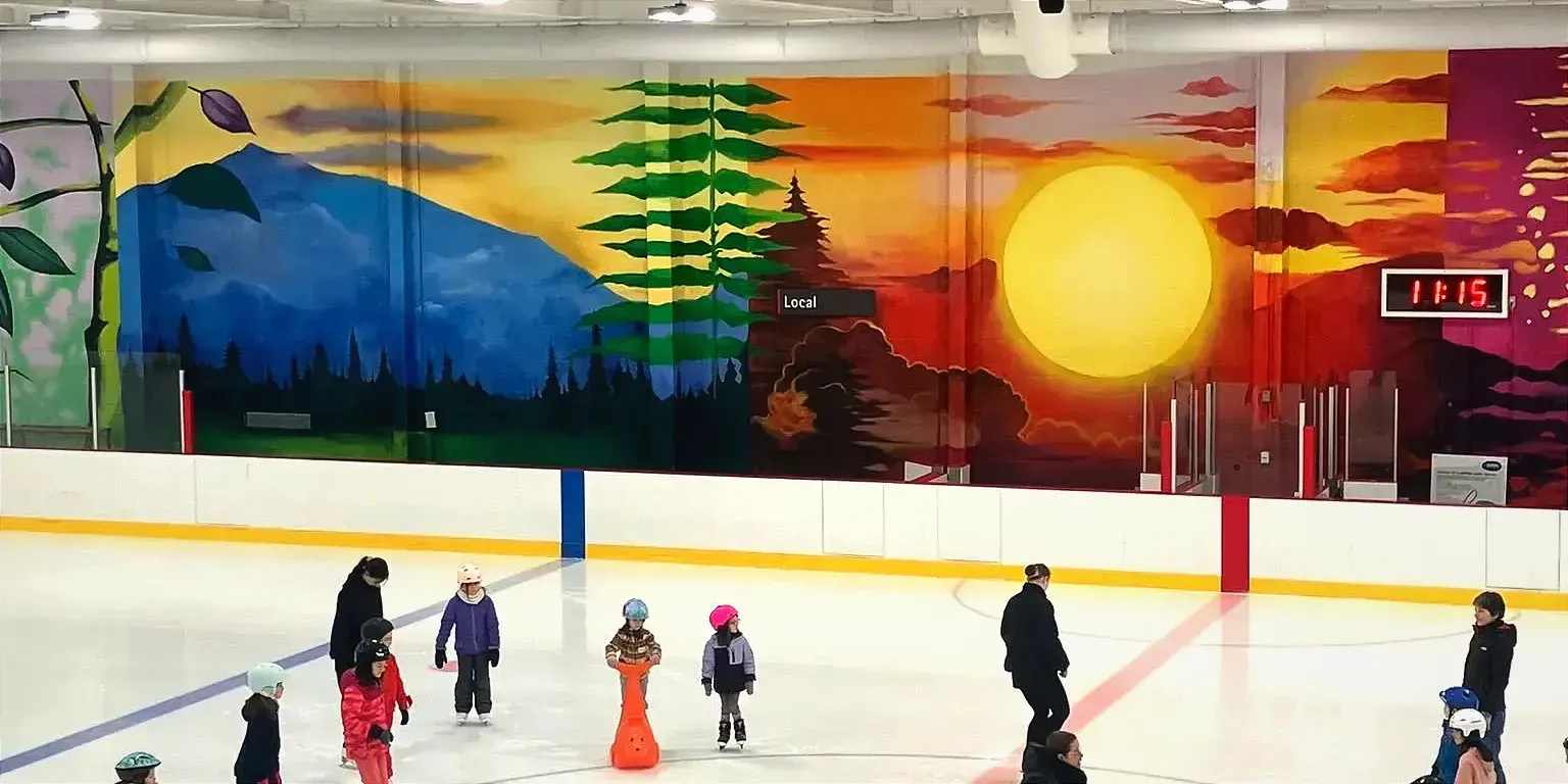 Une murale aux couleurs chaudes, illustrant un coucher de soleil, une montagne et des paysages naturels, domine le mur derrière le banc des joueurs de l'aréna. 