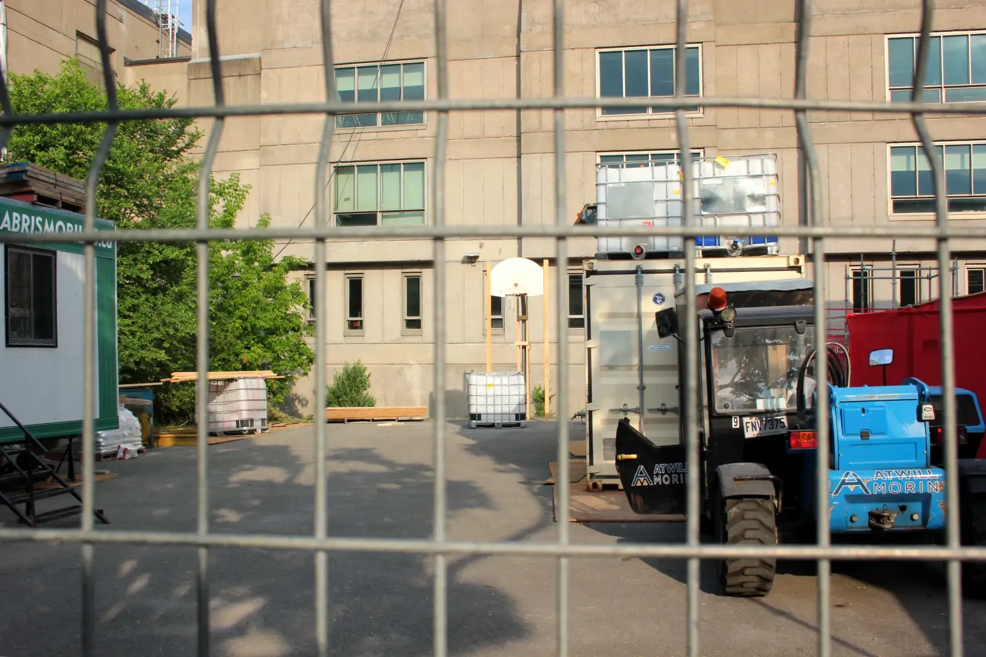 Un panier sans filet se trouve au fond d'une zone de construction, devant un mur de l'école Jeanne-Mance. 