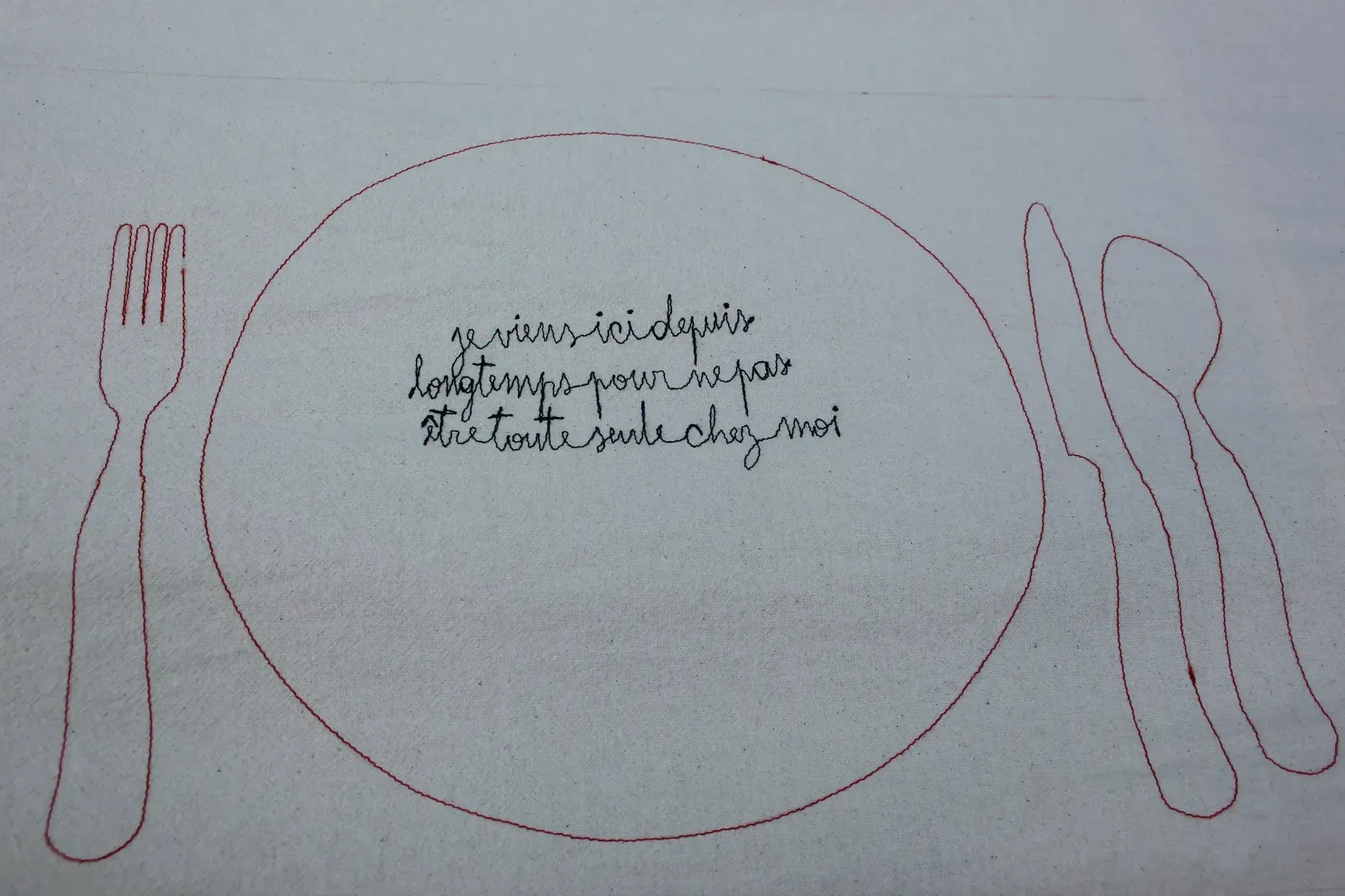 Le message est brodé en lettres attachées, à l'intérieur d'un cercle, rappelant la forme d'une assiette, entouré de formes d'ustensiles.