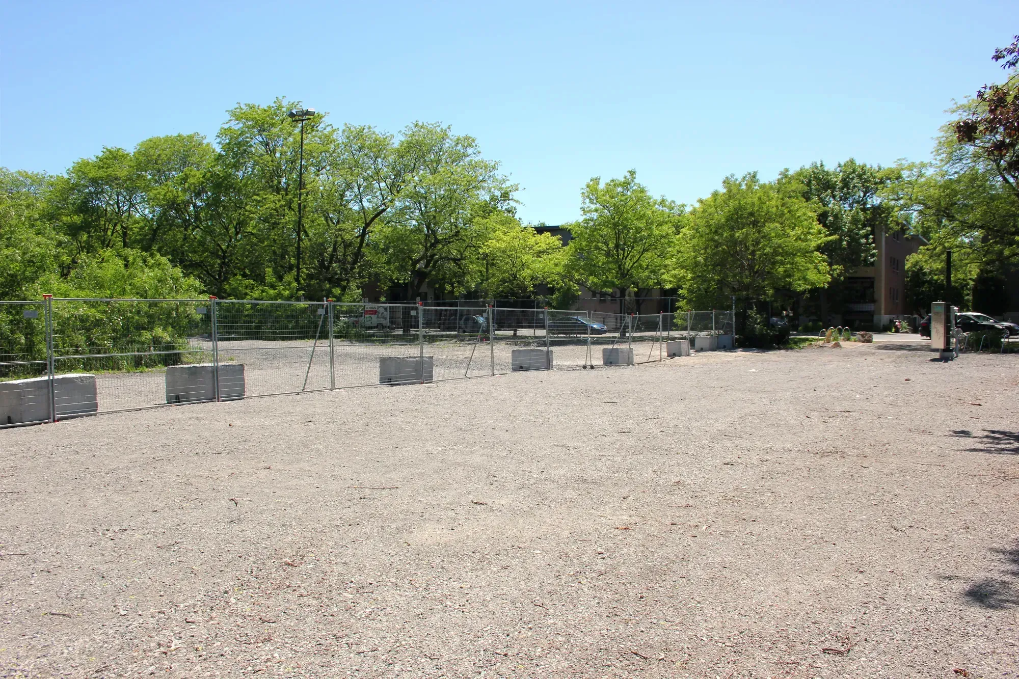 Des clôtures temporaires et des blocs de béton séparent une section du parc recouverte de gravier en deux.
