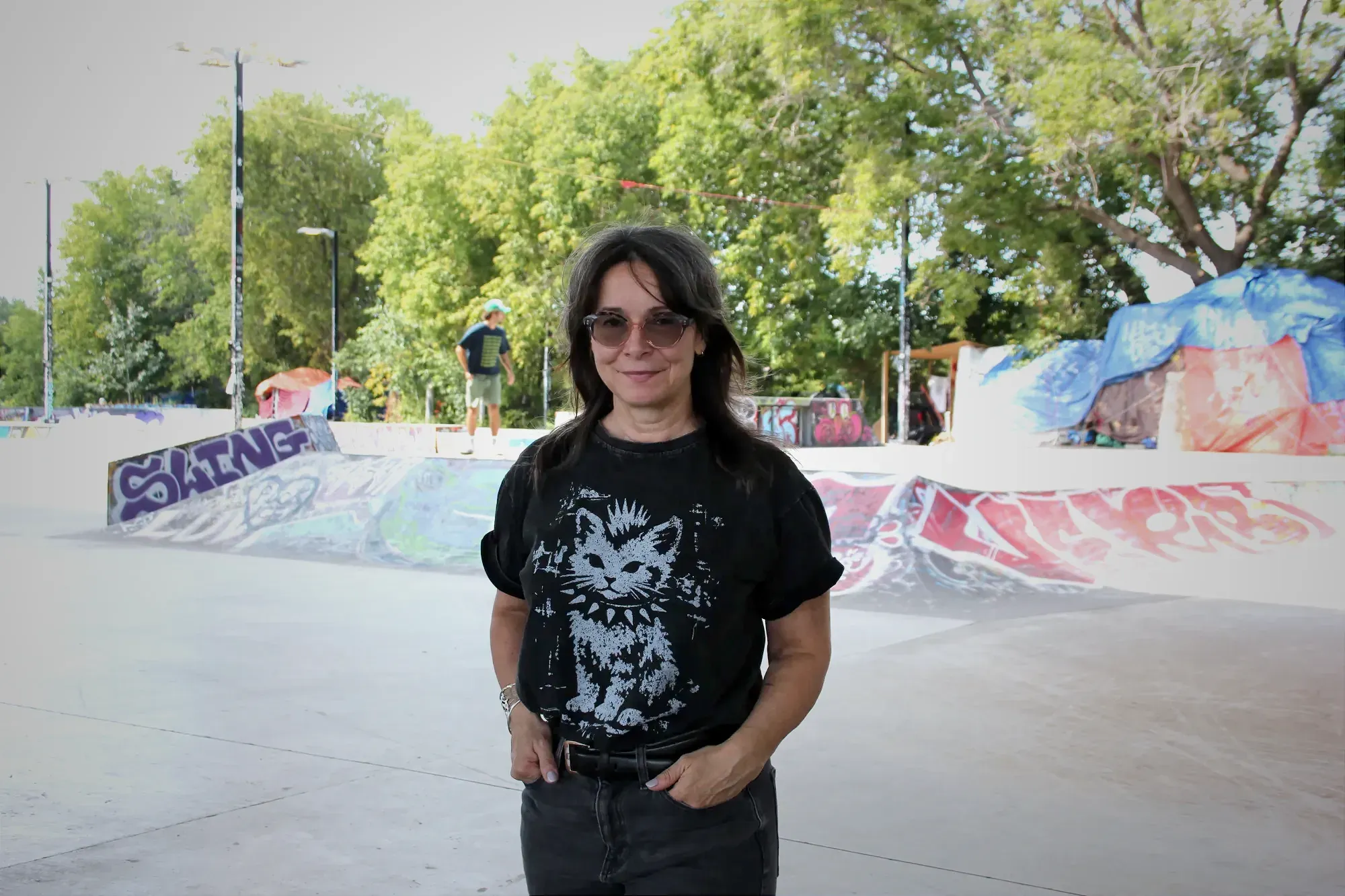 Marie Plourde pose sur le site du skatepark Van Horne. On peut voir deux campements derrière elle, ainsi qu'un planchiste qui s'aventure sur le site. 