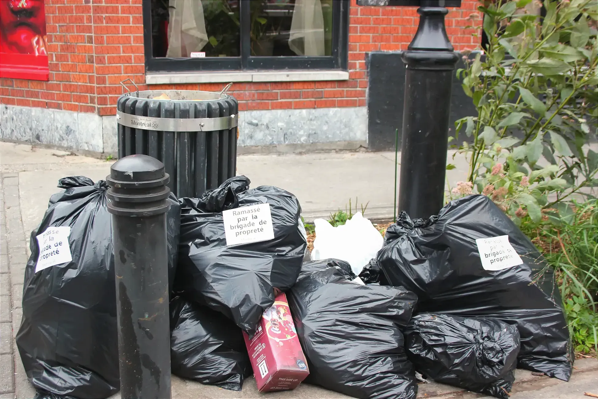 Quelques sacs de vidanges traînent près d'une poubelle publique de coin de rue. Ils sont tous marqués d'un collant sur lequel on peut lire «Ramassé par la brigade de propreté».