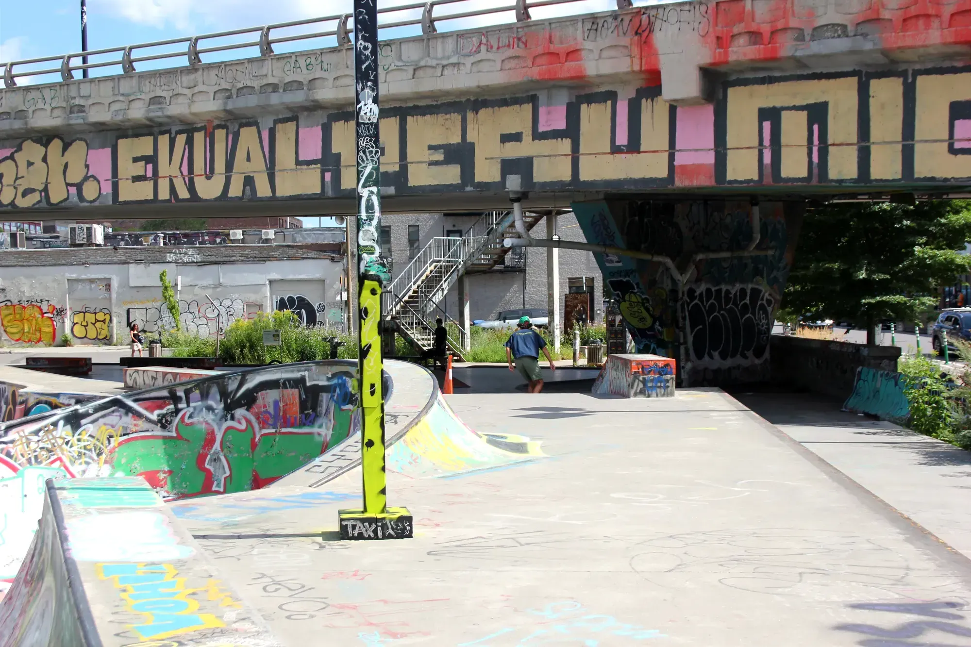 Un planchiste d'éloigne de la caméra, descedant une pente vers la zone du skatepark qui passe sous le viaduc Van Horne-Rosemont. 