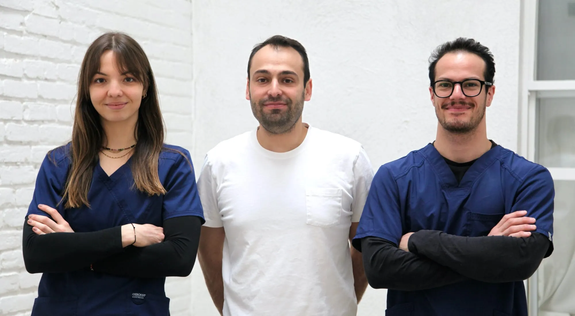 Un homme habillé en blanc est entouré d'une femme et d'un homme souriant, en uniforme bleu et noir.