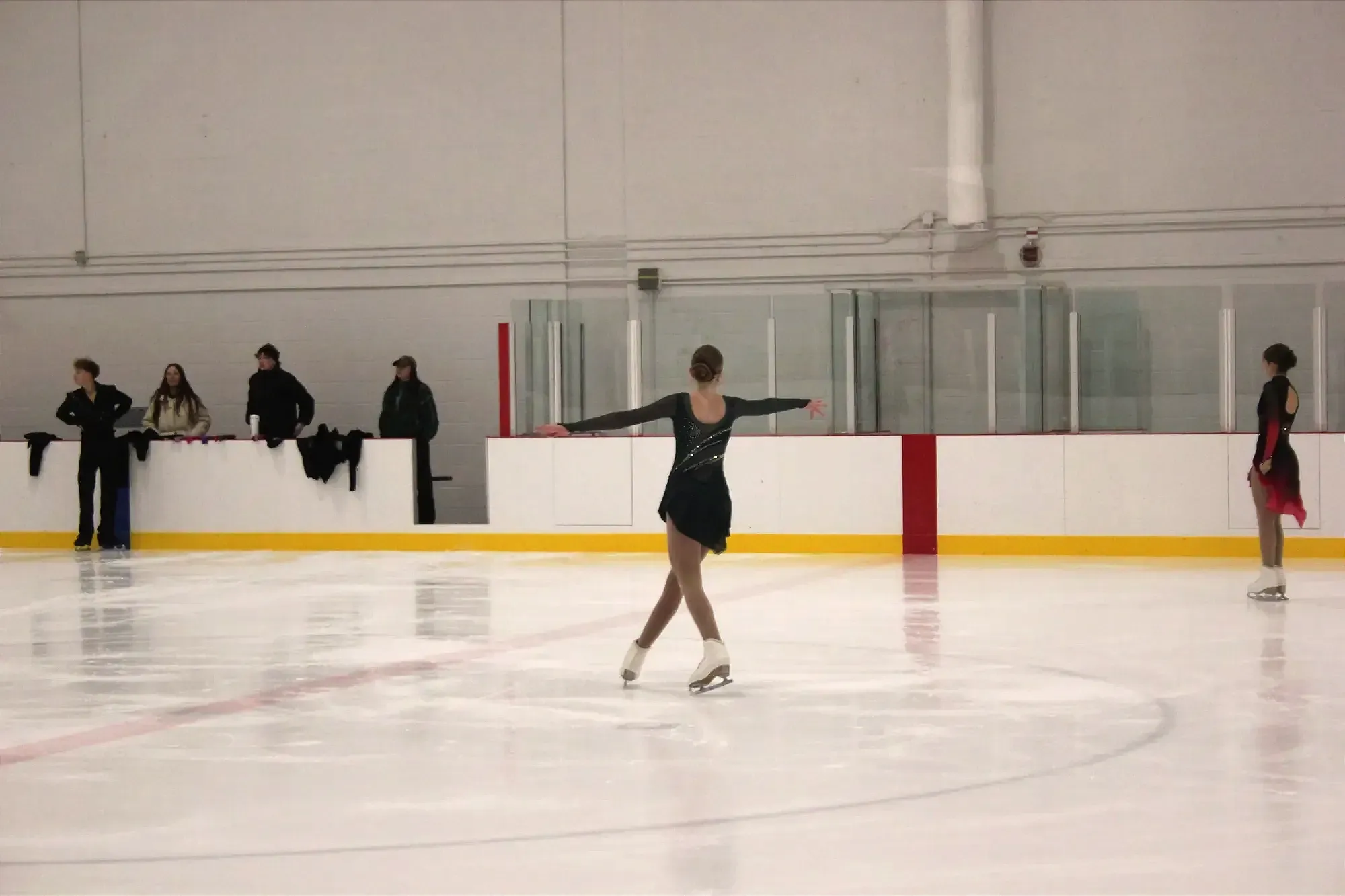 Une patineuse artistique au centre de la patinoire s'apprête à tourner sur elle-même, alors que d'autres patineurs de fantaisie sont dans les parages.