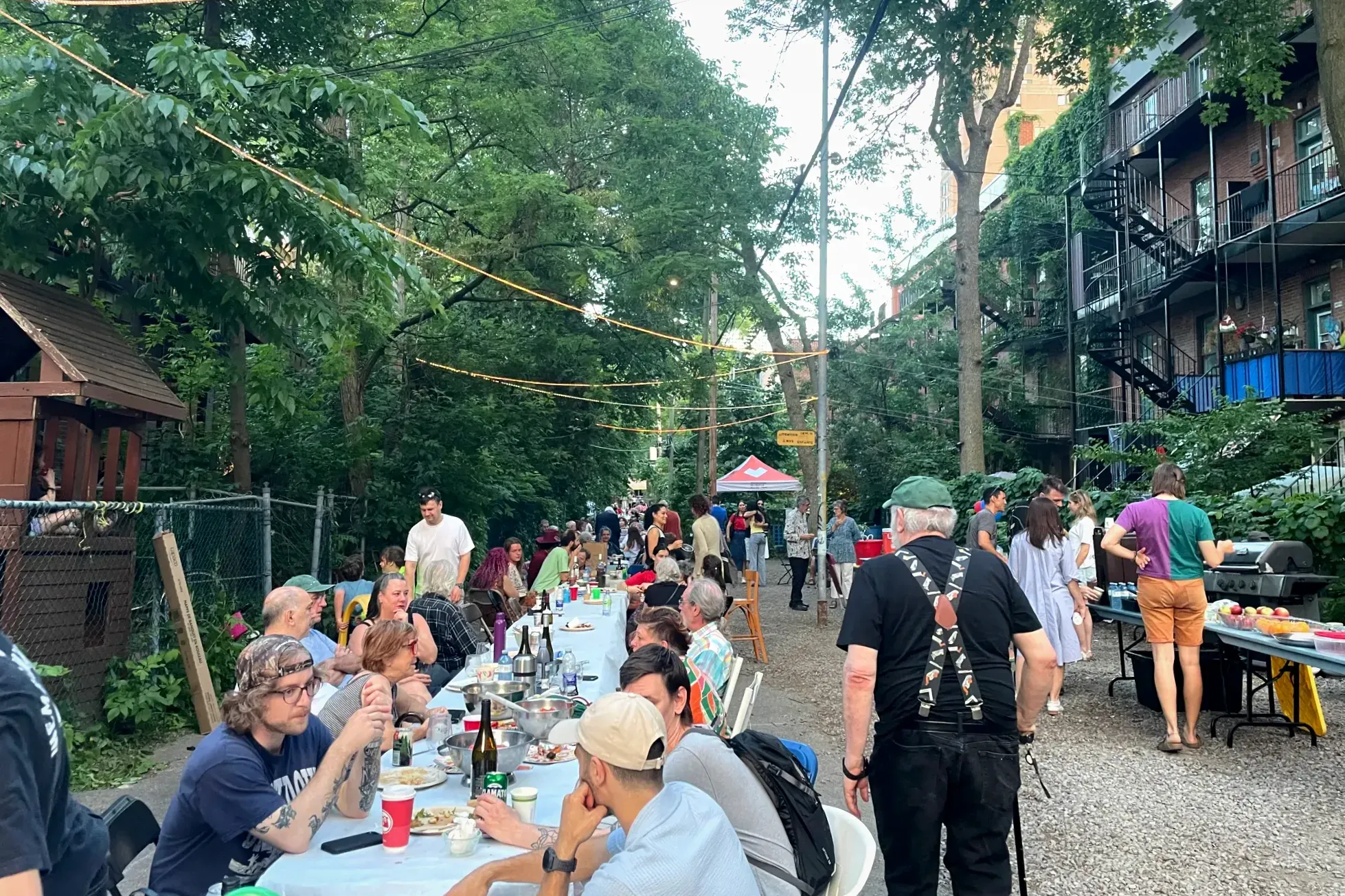 Plusieurs dizaines de personnes sont assis autour d'une longue table qui s'étire vers le fond de la ruelle, alors que quelques autres se serevent au buffet à droite.