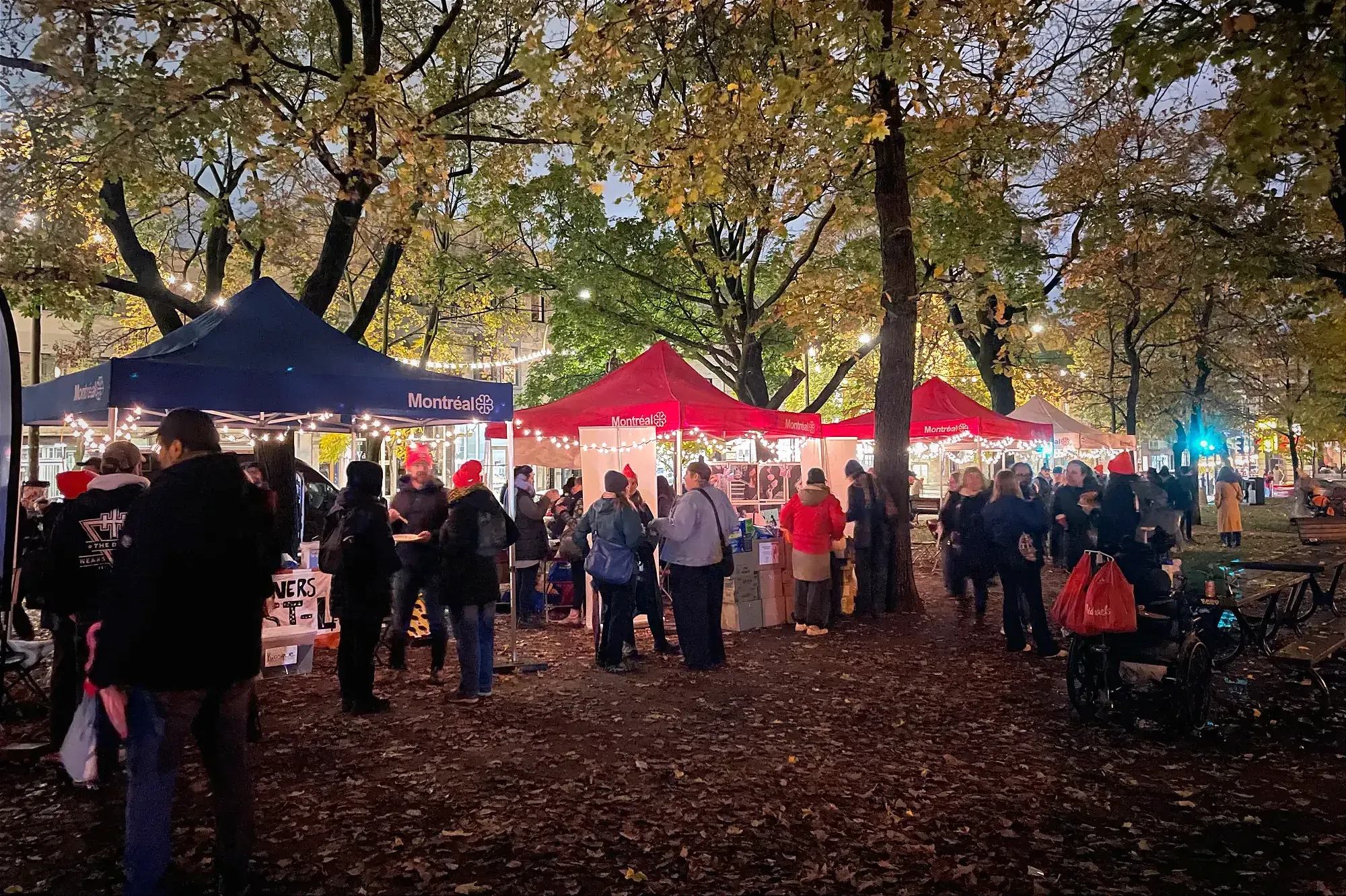 Des kiosques temporaires sont entourés de personnes et ornées de lumières décoratives dans le parc Lahaie. 