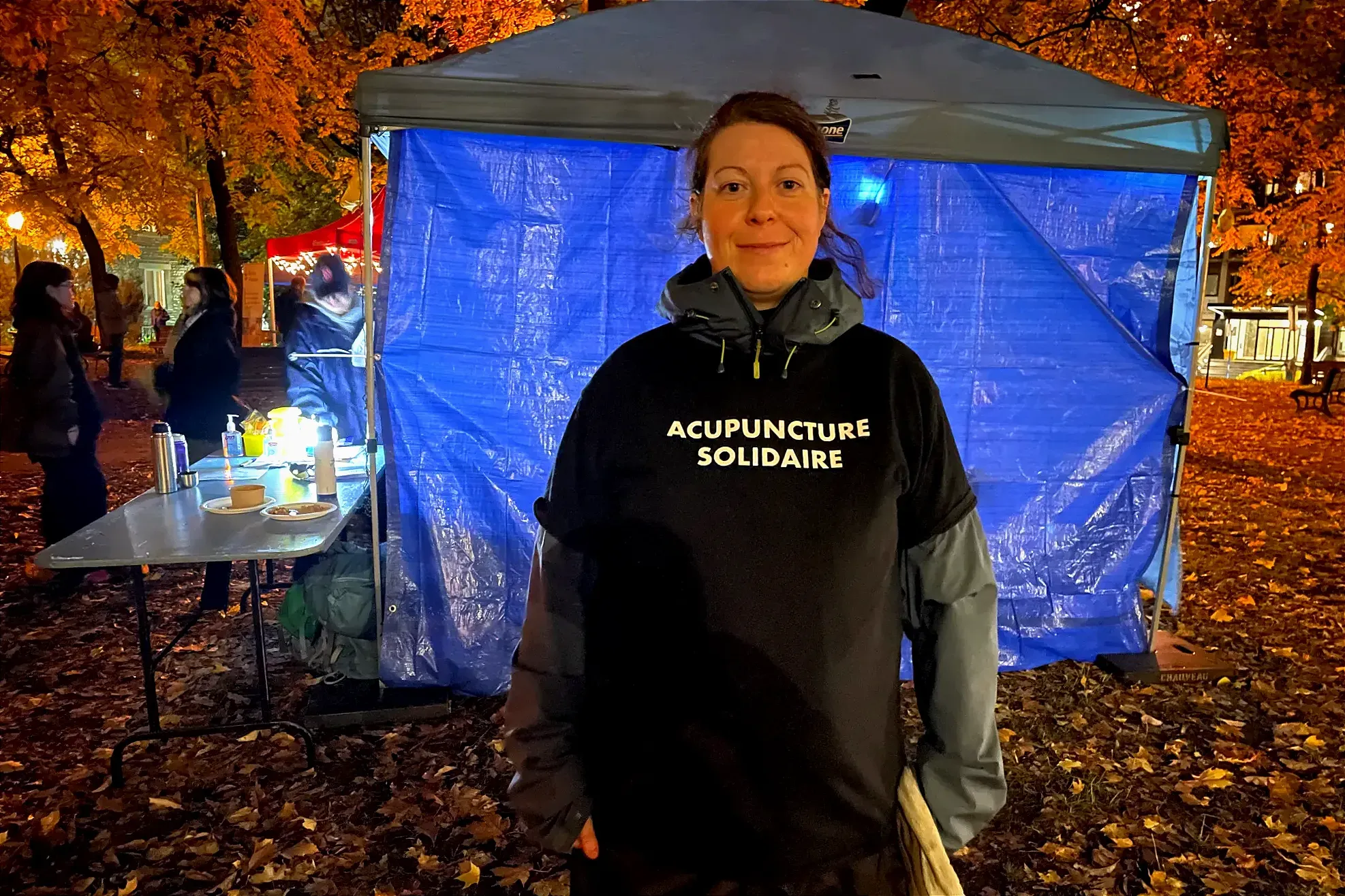 Myro Le Ber Assiani, acupuncteur·e, pose devant le kiosque de Dans la rue, au parc Lahaie, avec son t-shirt «Acupuncture solidaire».