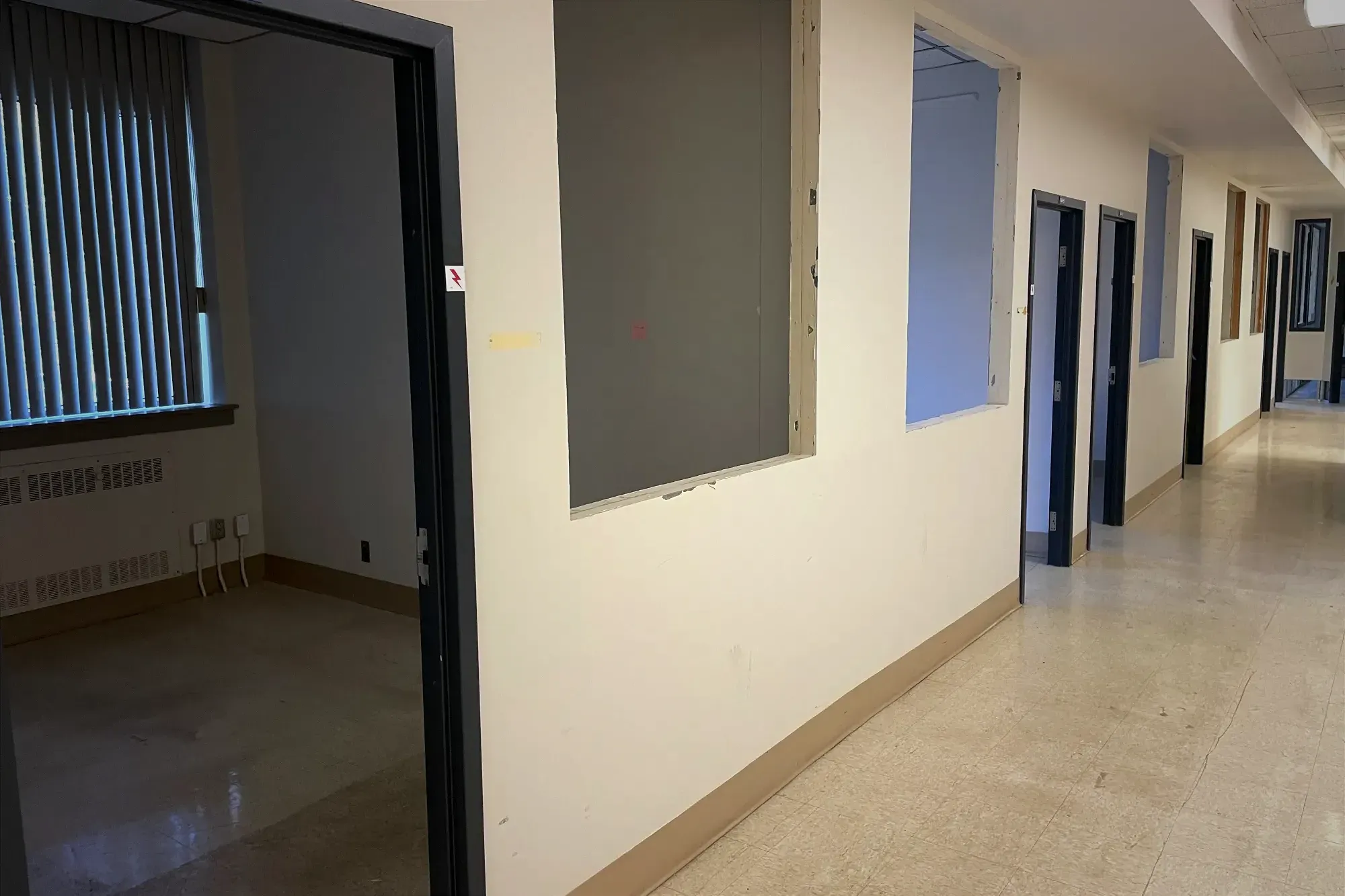 On peut distinguer plusieurs cadres de porte sans porte et de trous qui attendent d'être remplis par des fenêtres dans un corridor d'un milieu aux airs administratifs.